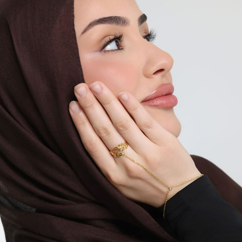 Photo of the model's right hand touching their right cheek. The model is wearing the gold Palestine Olive Hand Chain on their right middle finger.