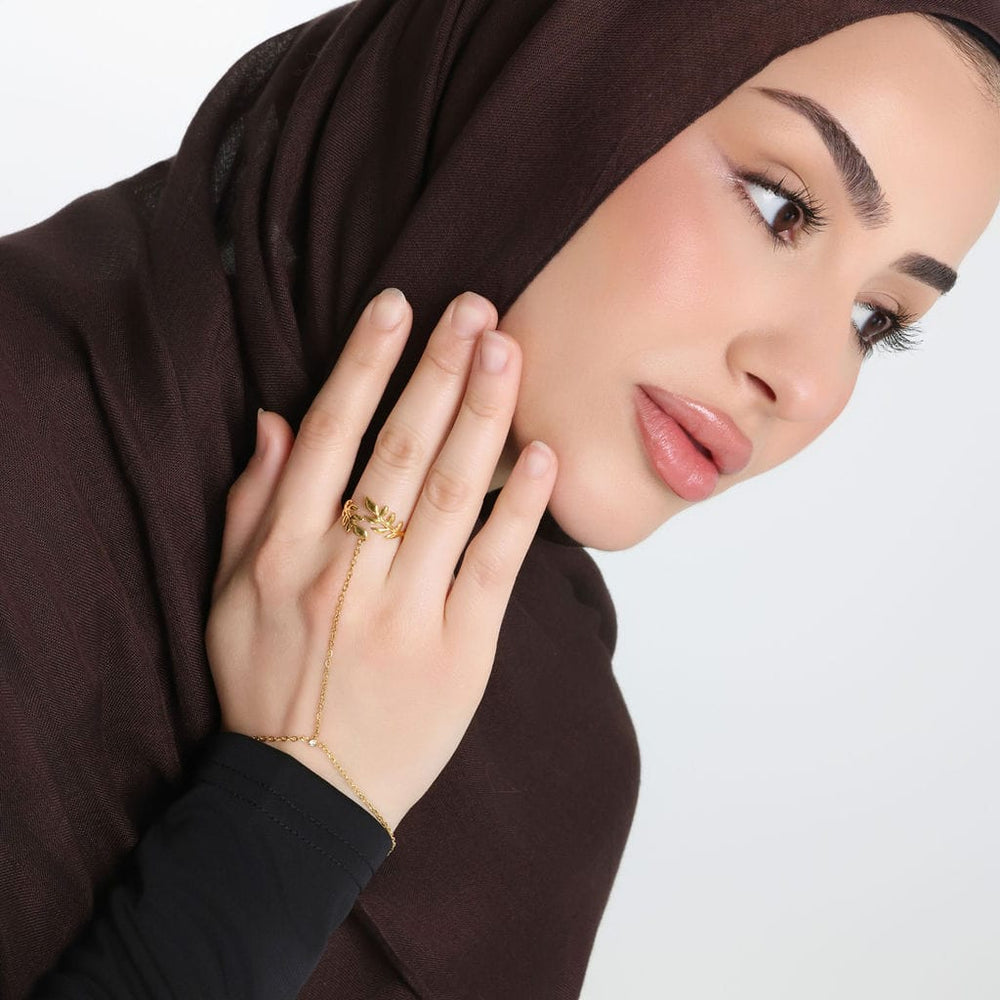 Photo of the right side profile of the model. The model is touching their right cheek with their right hand. The model is wearing the gold Palestine Olive Hand Chain on their right middle finger.