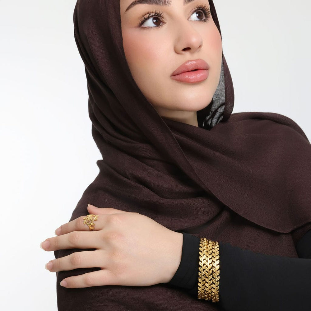 Photo of the model touching their right shoulder with their left hand to show the three pieces of gold Palestine Olive Layering Bangle they are wearing.