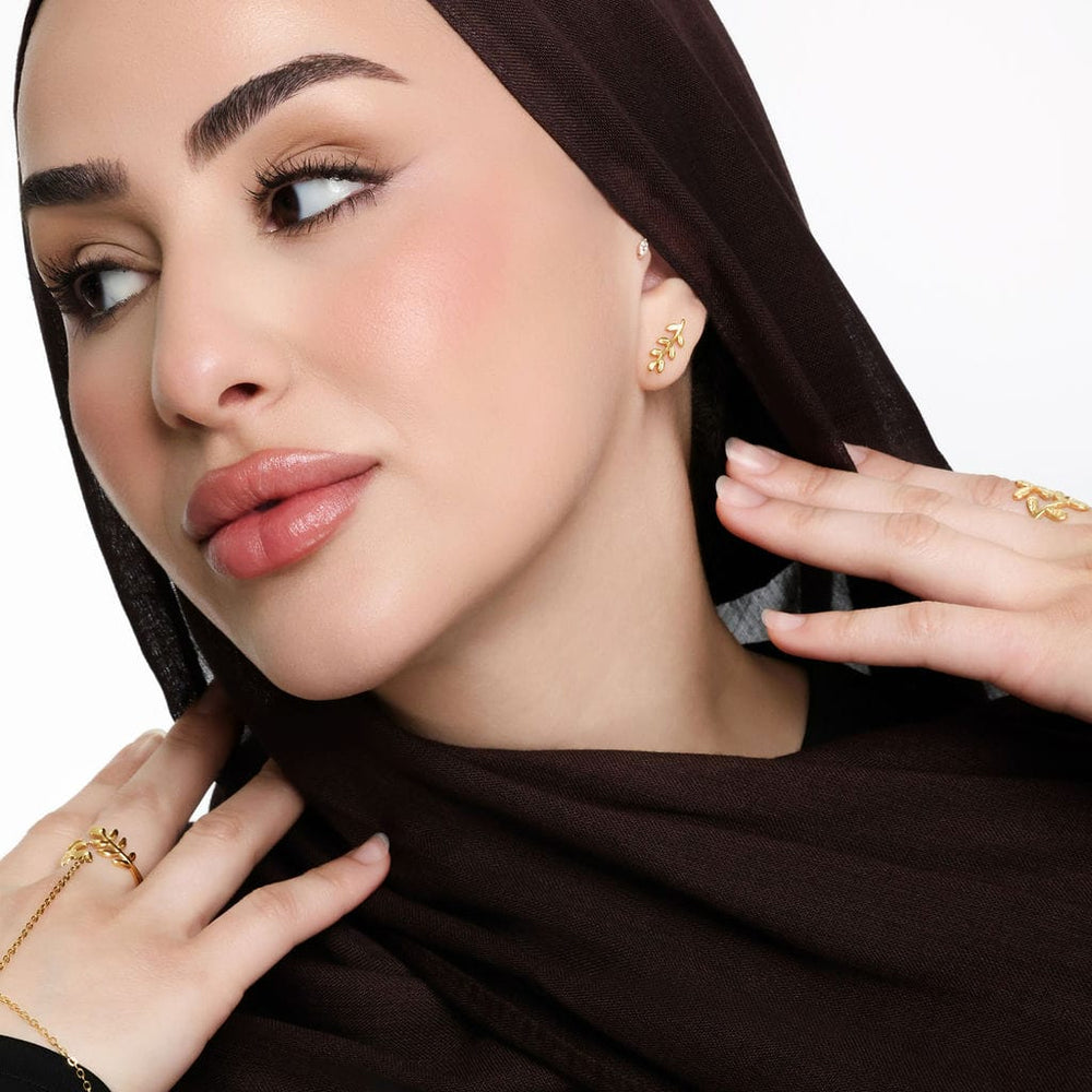 Photo of the model leaning their head to the side to show the gold Palestine Olive Leaf Earrings they are wearing on their left ear.