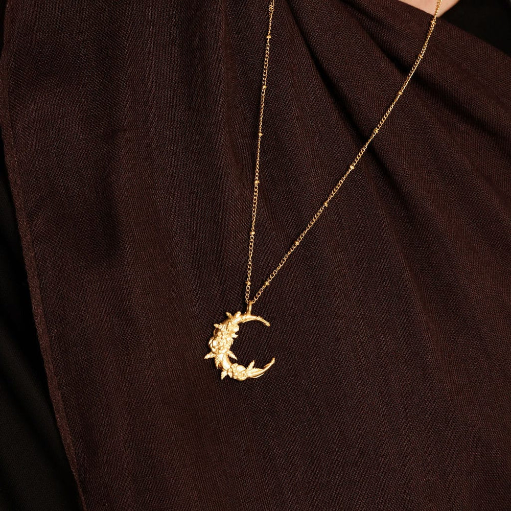 Close up of the gold Palestine Poppy Crescent Necklace against the brown fabric of the model's clothing.