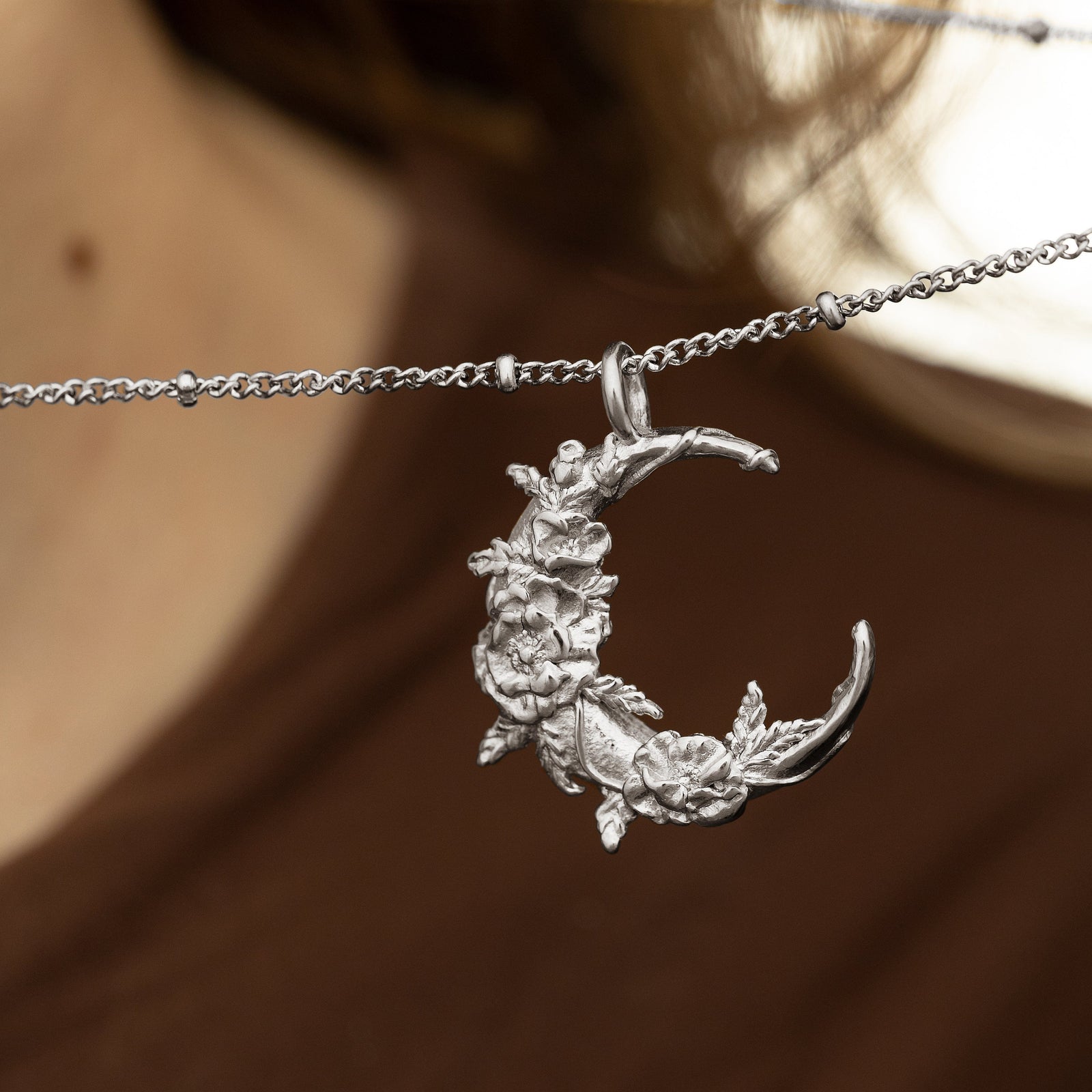 Photo of the silver Palestine Poppy Crescent pendant hanging on the thin dotted necklace.