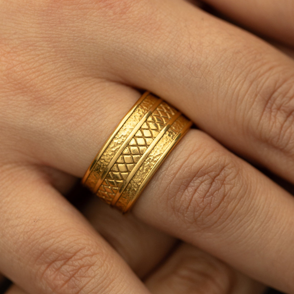 Woman wearing the gold Palestine Tribute Ring with textured edges and a diamond-patterned center on her finger in a close-up shot.