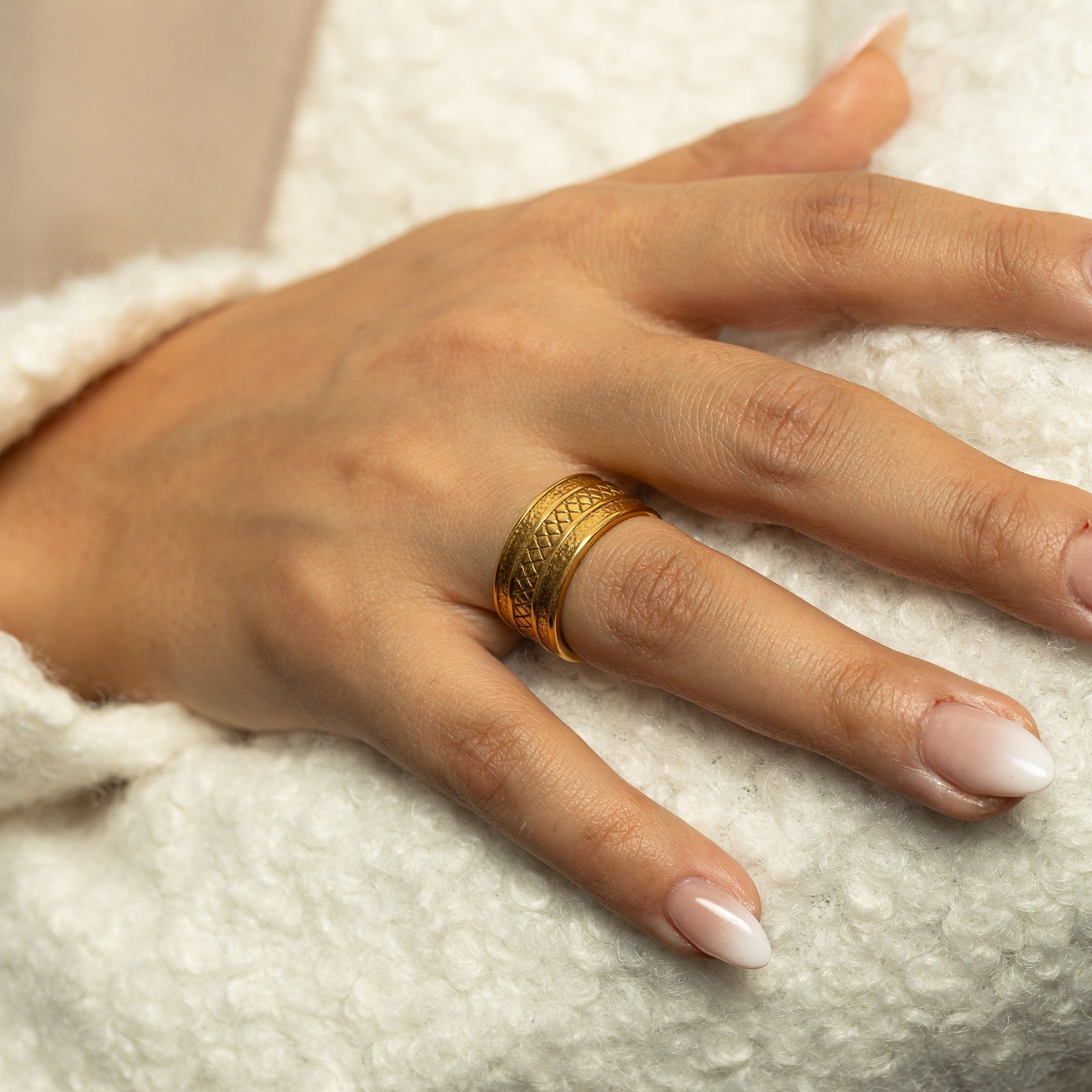 Woman wearing the gold Palestine Tribute Ring with textured edges and a diamond-patterned center on her finger in a close-up shot.