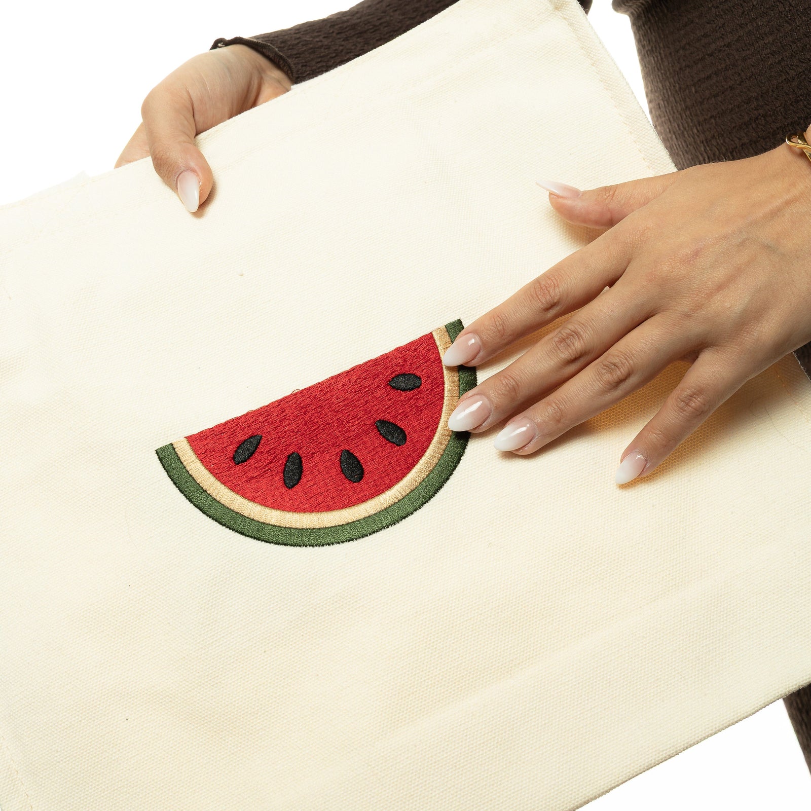 Photo of the model holding the Palestine Watermelon Tote, left hand touching the embroidered watermelon art.