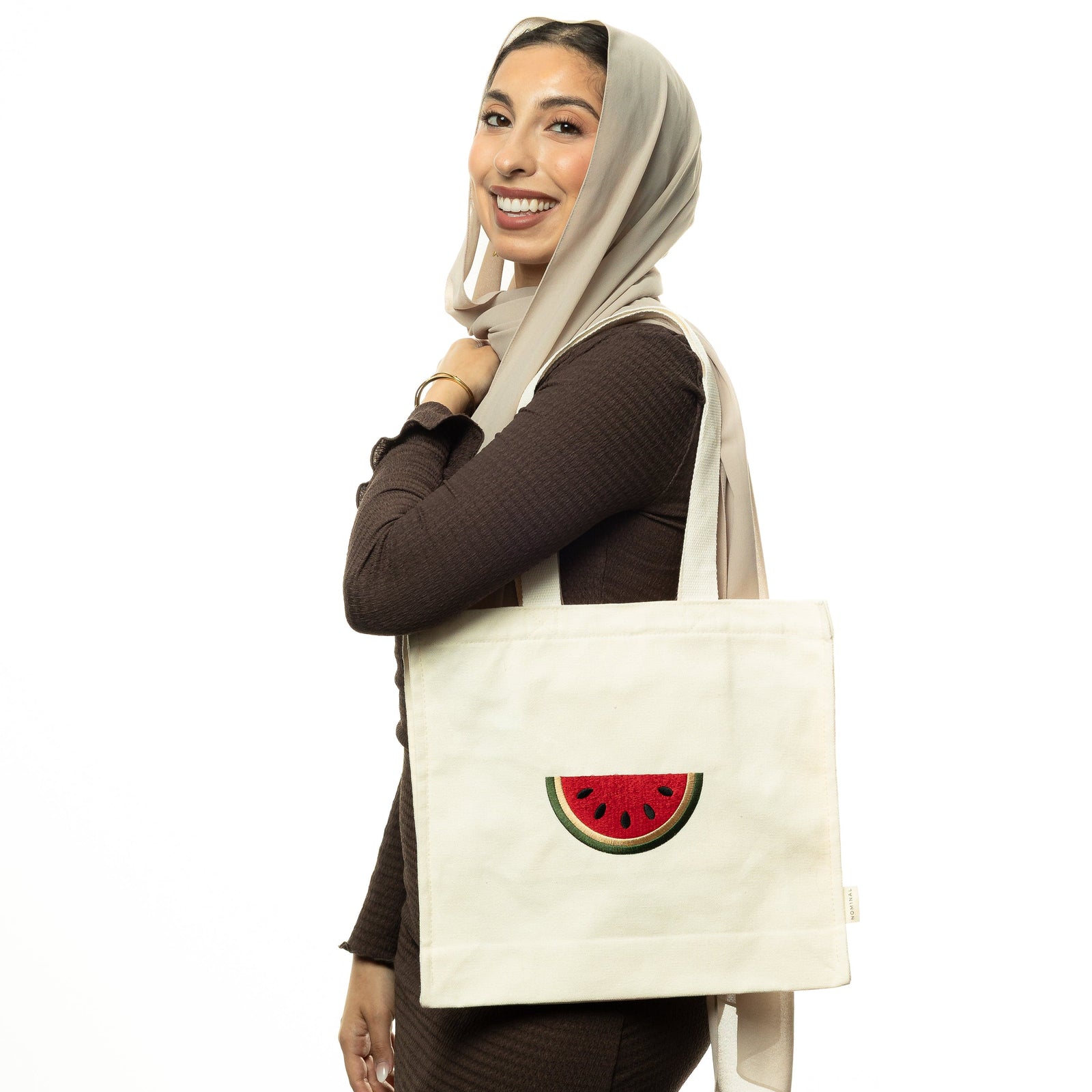 Photo of the model smiling to the camera while carrying the Palestine Watermelon Tote on their left shoulder.
