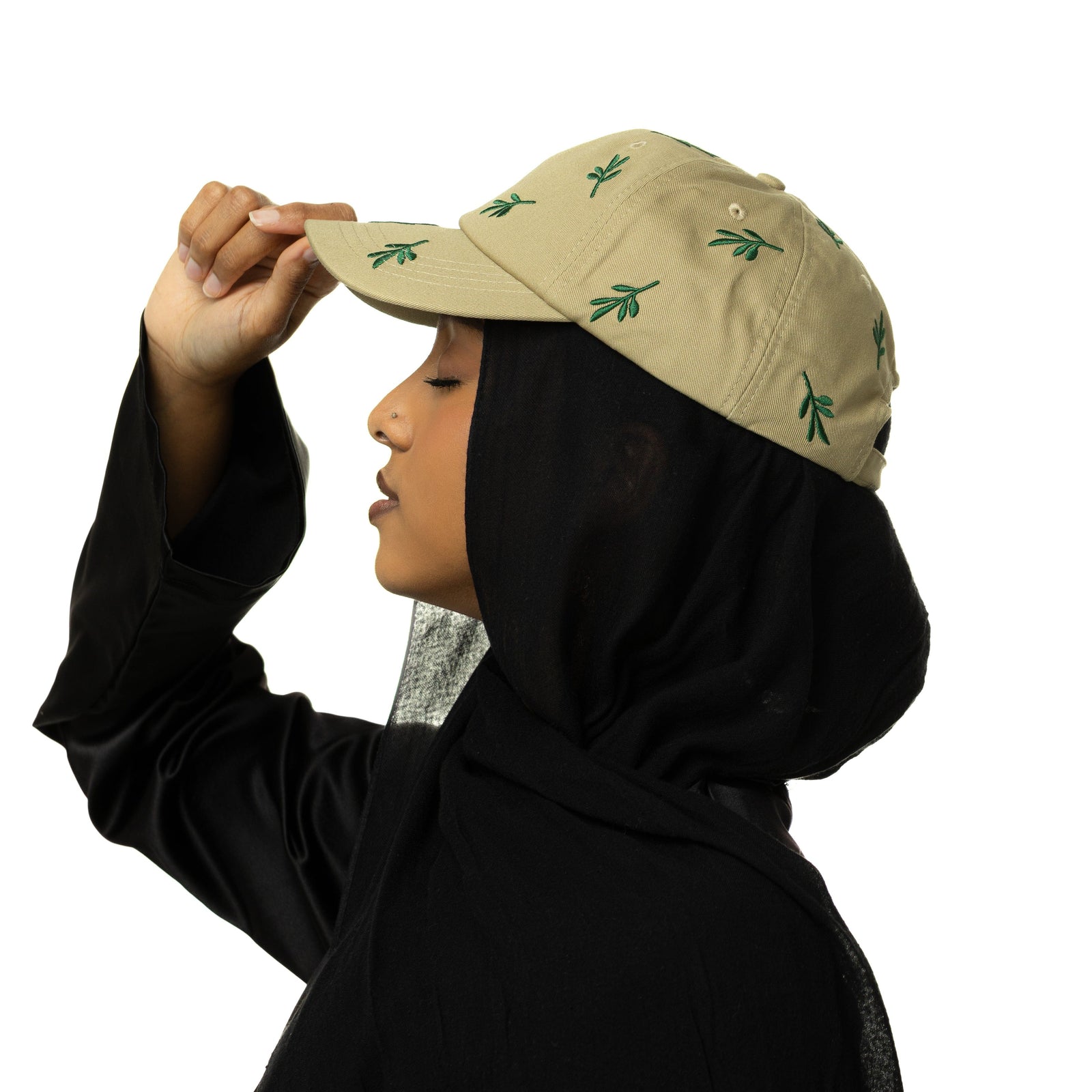 Sie profile photo of the model wearing the beige Palestinian Olive branch with green olive branch embroidery. The model is holding the tip of the cap.