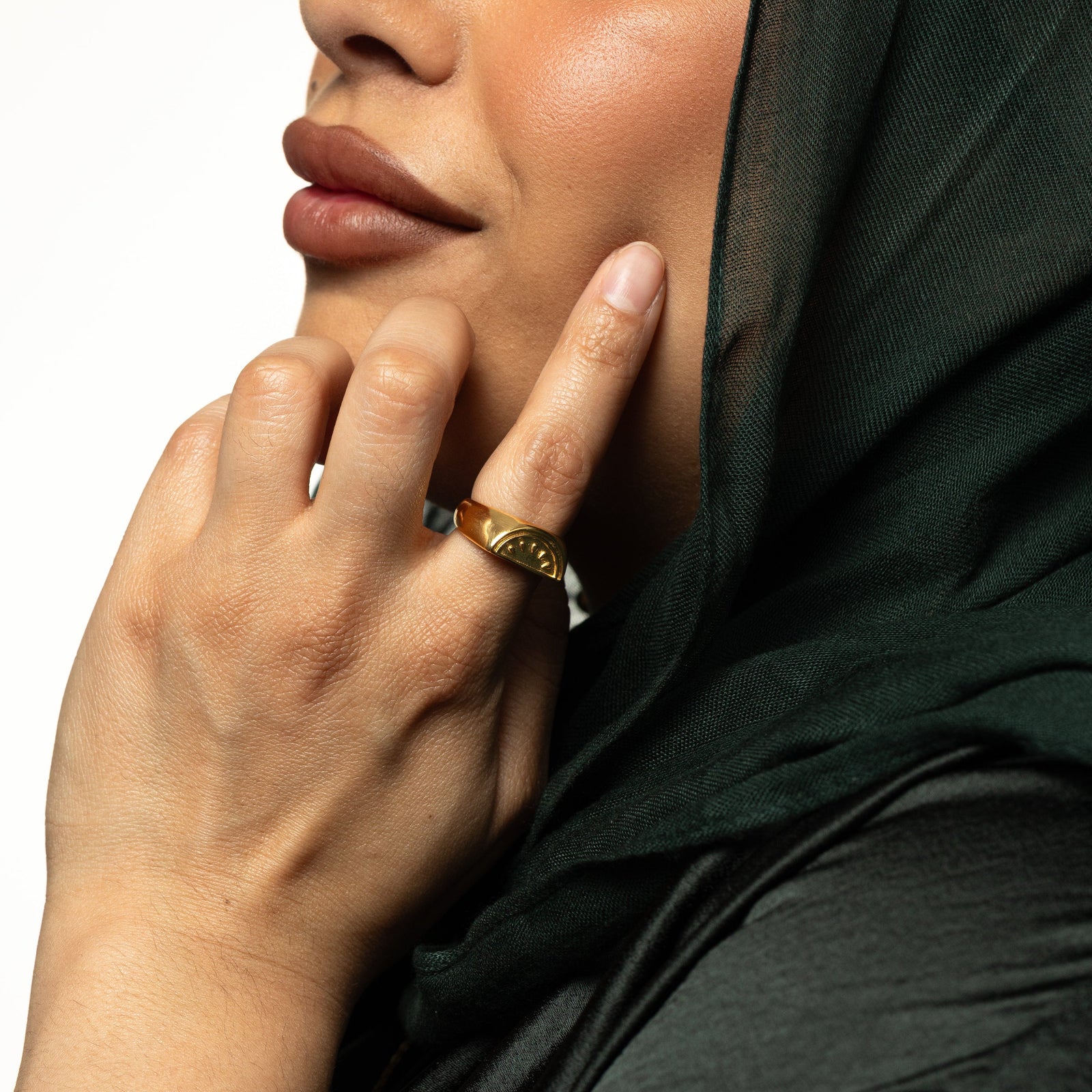 Model touching their face with their hand. The model is wearing the gold Palestinian Watermelon Ring on their index finger.