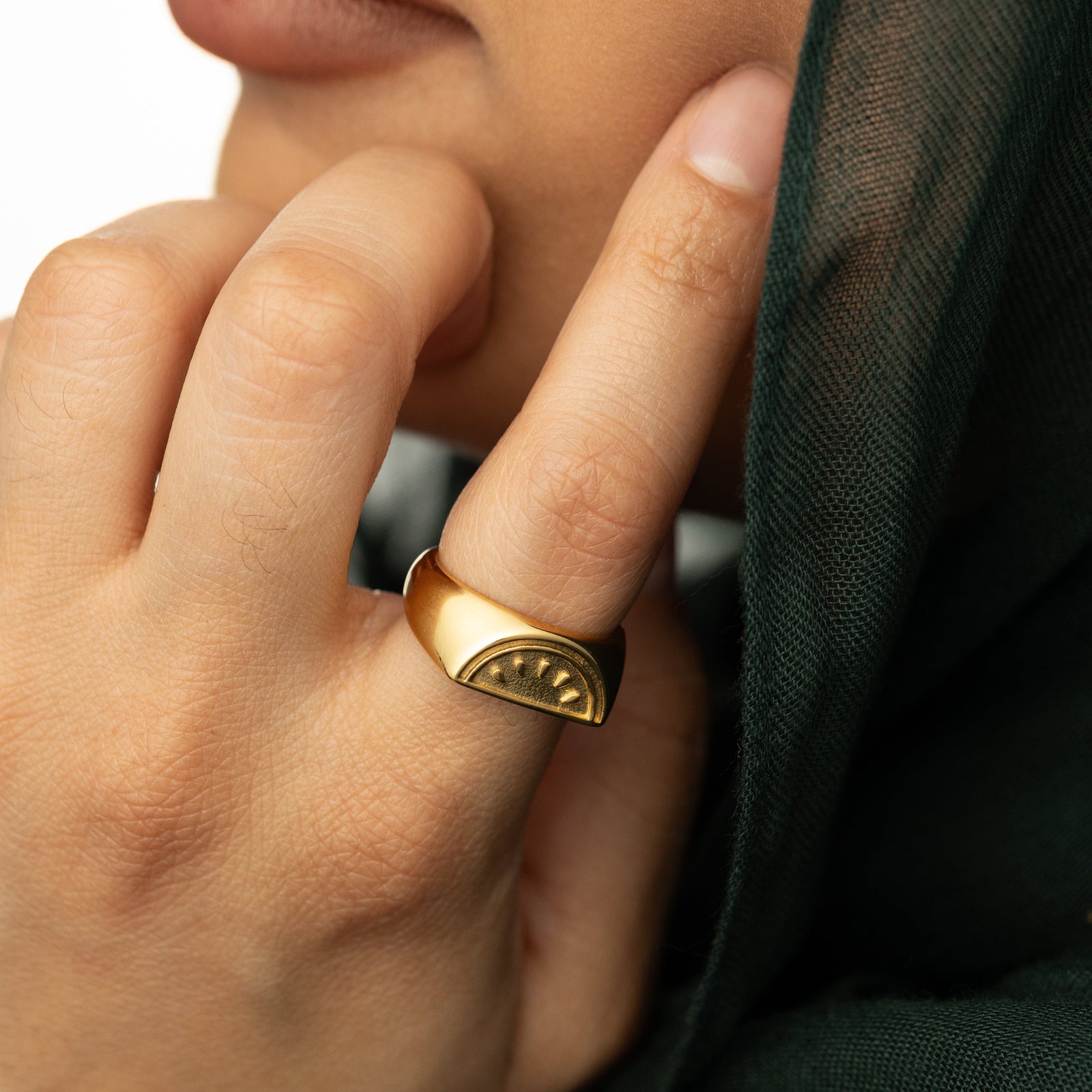 Close up photo of the model touching their face with their hand. The model is wearing the gold Palestinian Watermelon Ring on their index finger.