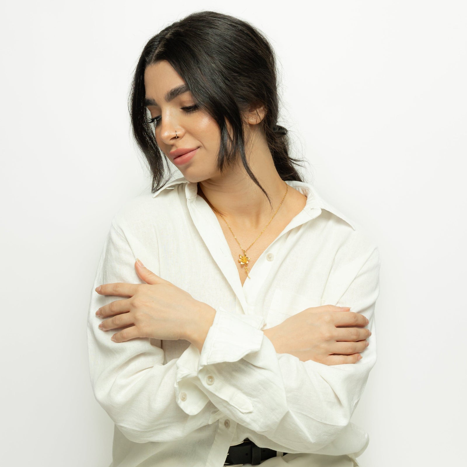 Photo of the model looking down with her arms across her body. The model is wearing the gold Passion' Lily Necklace.