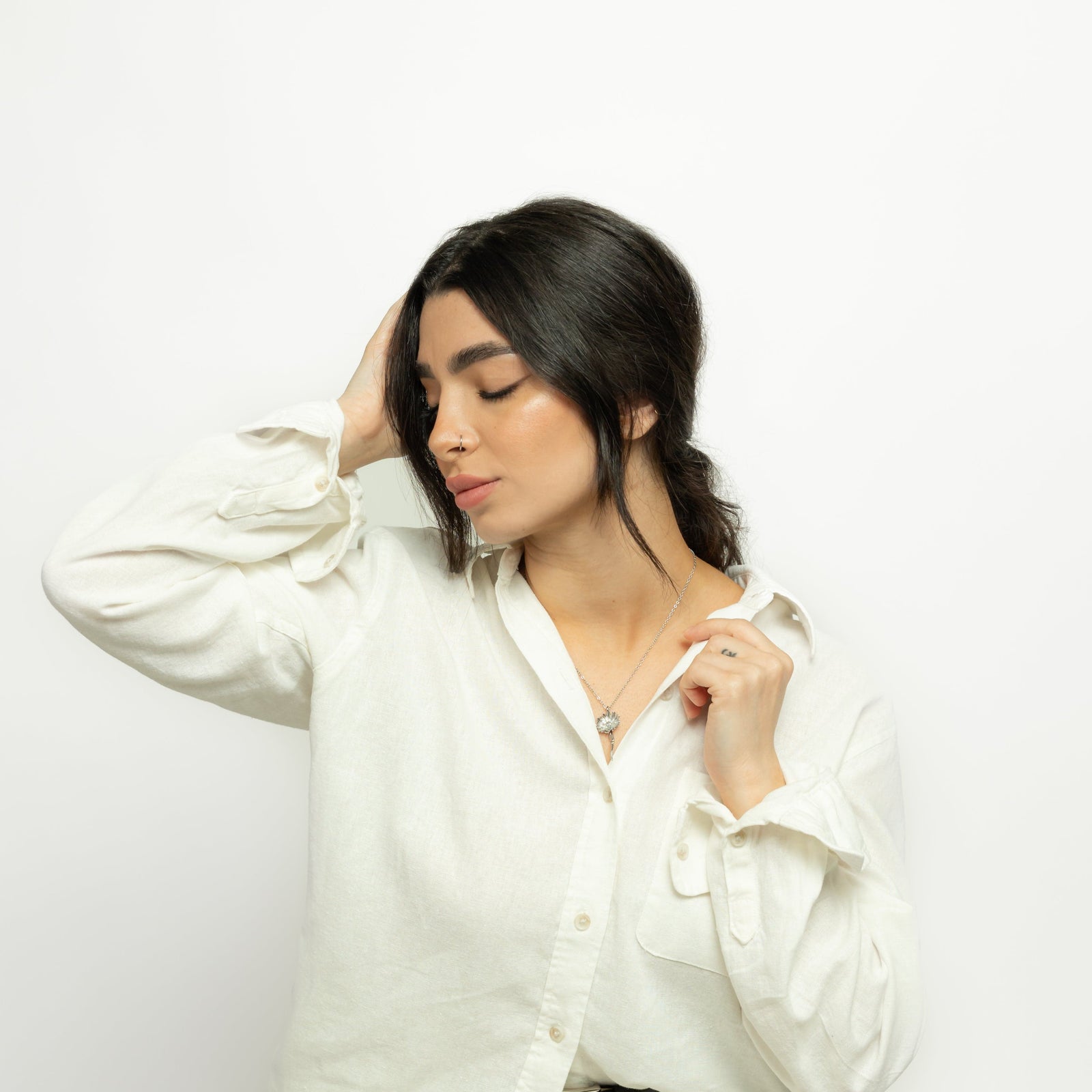 Photo of the model with their eyes closed and right hand holding their head. The model is wearing the silver Patience' Aster Necklace.