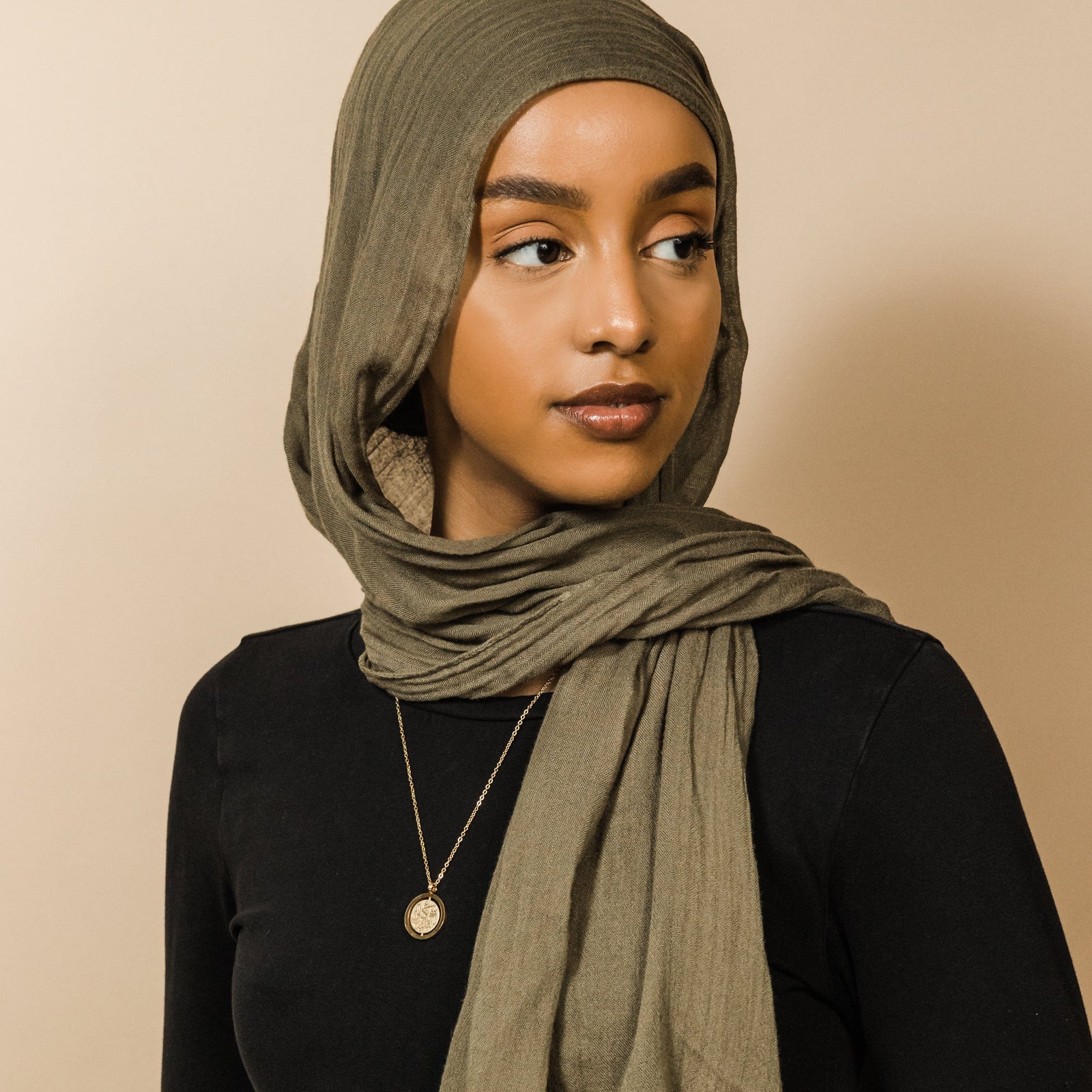 Photo of the model looking away from the camera. The model is wearing the gold Everything Comes with Patience Necklace.