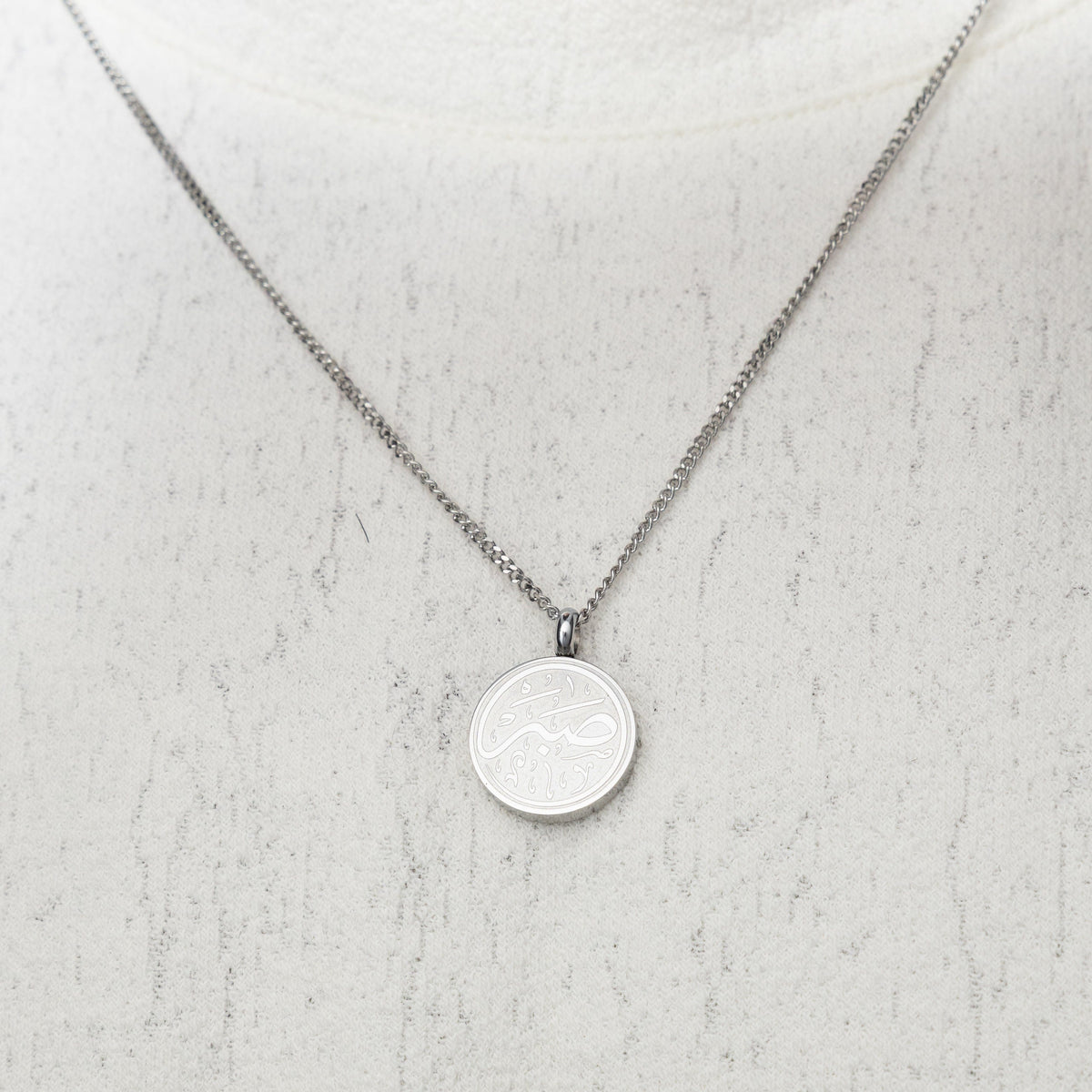 Silver Patience Token necklace worn on a white textured top.