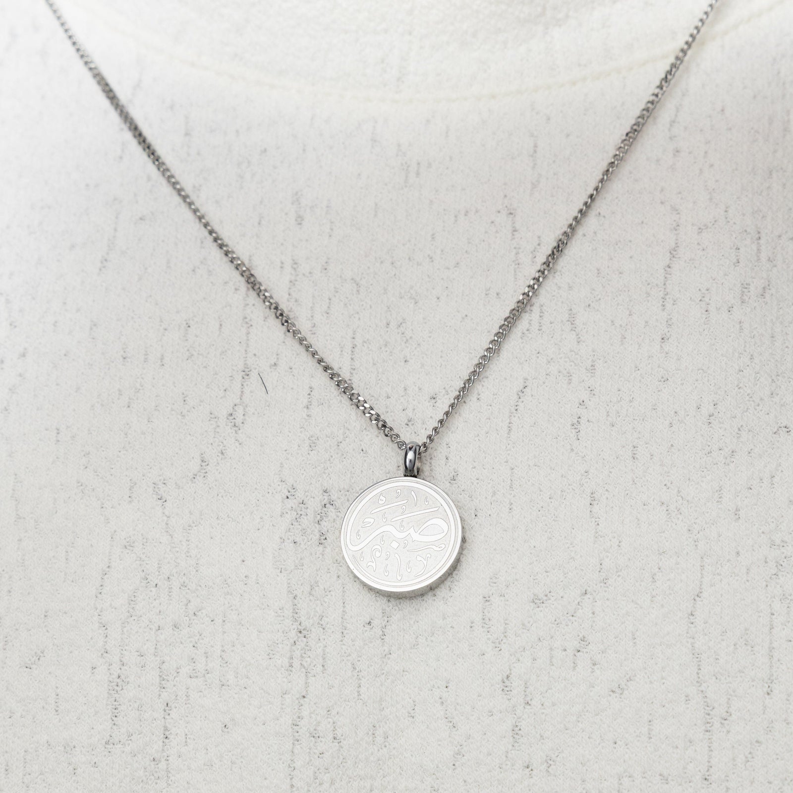 Silver Patience Token necklace worn on a white textured top.