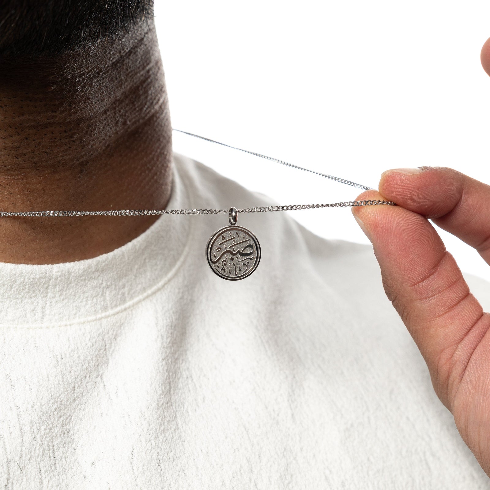 Man holding up a silver patience token necklace, worn over a white shirt.
