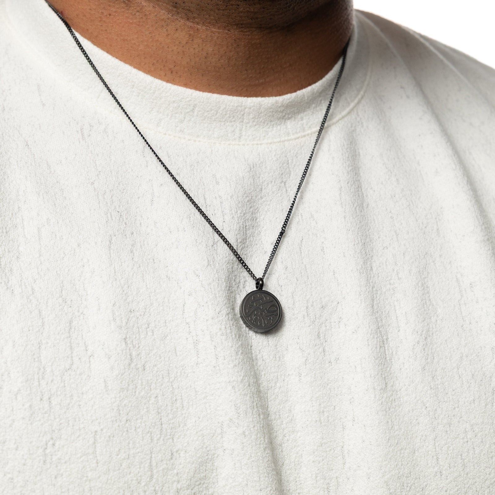 Black Patience Token necklace worn over a white textured shirt.