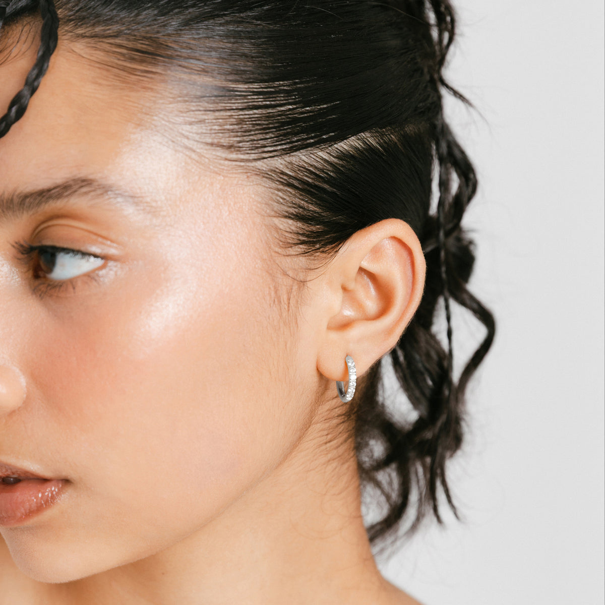 Model wearing a silver 12mm Pavé Huggie Hoop set with clear crystals.   