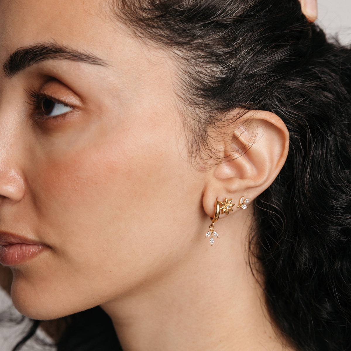 Model styled in 18k gold-plated Nominal jewelry featuring an ear stack with the Pavé Olive Branch Huggies, Bezel Bloom Studs, and Pavé Olive Branch Studs.