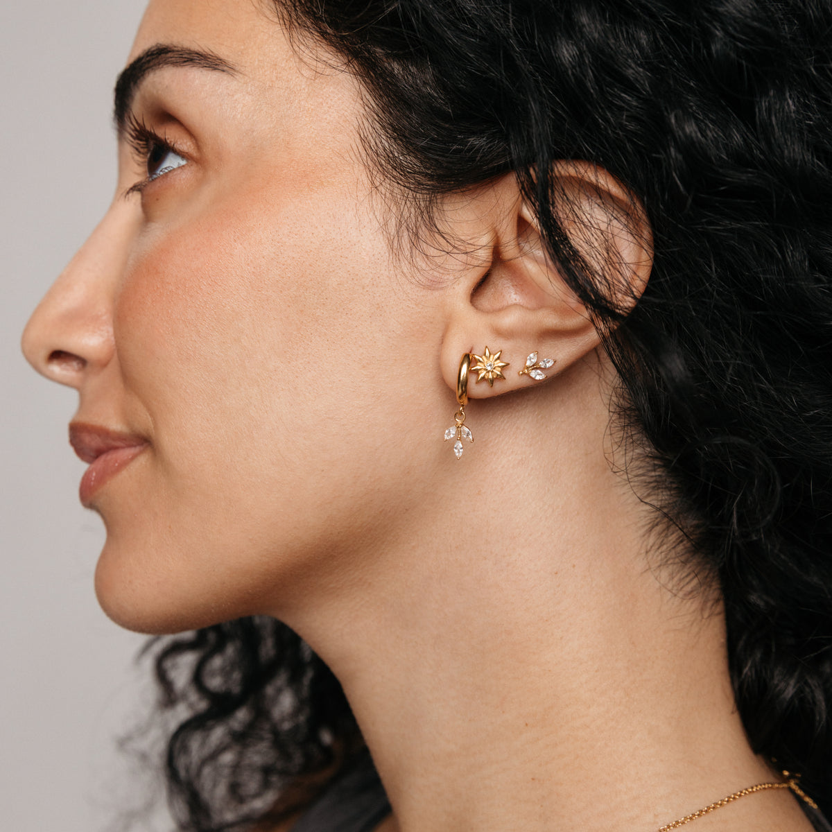 Model styled in 18k gold-plated Nominal jewelry featuring an ear stack centered on the Pavé Olive Branch Huggies, paired with the Bezel Bloom Studs and Pavé Olive Branch Studs.
