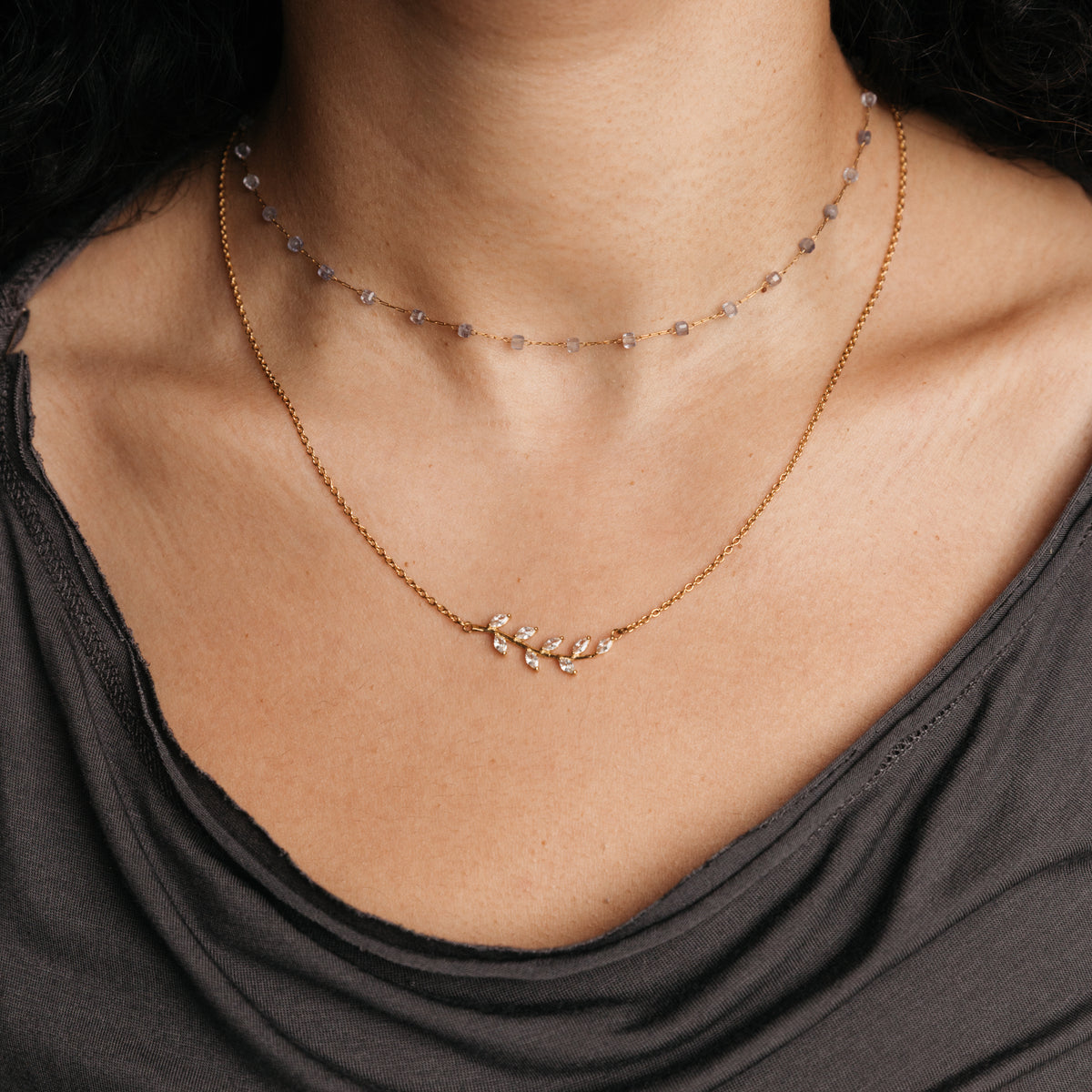 Model styled in layered 18k gold-plated Nominal jewelry featuring the Pavé Olive Branch Necklace paired with the Essential Iolite Micro Chain.