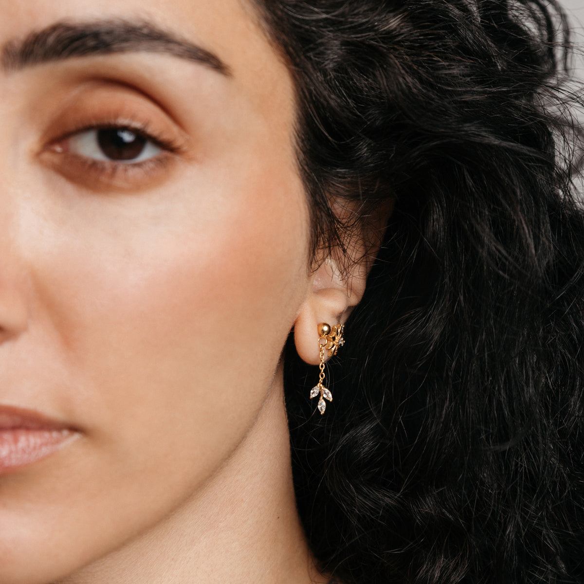 Model styled in 18k gold-plated Nominal jewelry featuring an ear stack with the Pavé Raining Olive Branch Drop Earrings, Bezel Bloom Studs, and Pavé Olive Branch Studs.