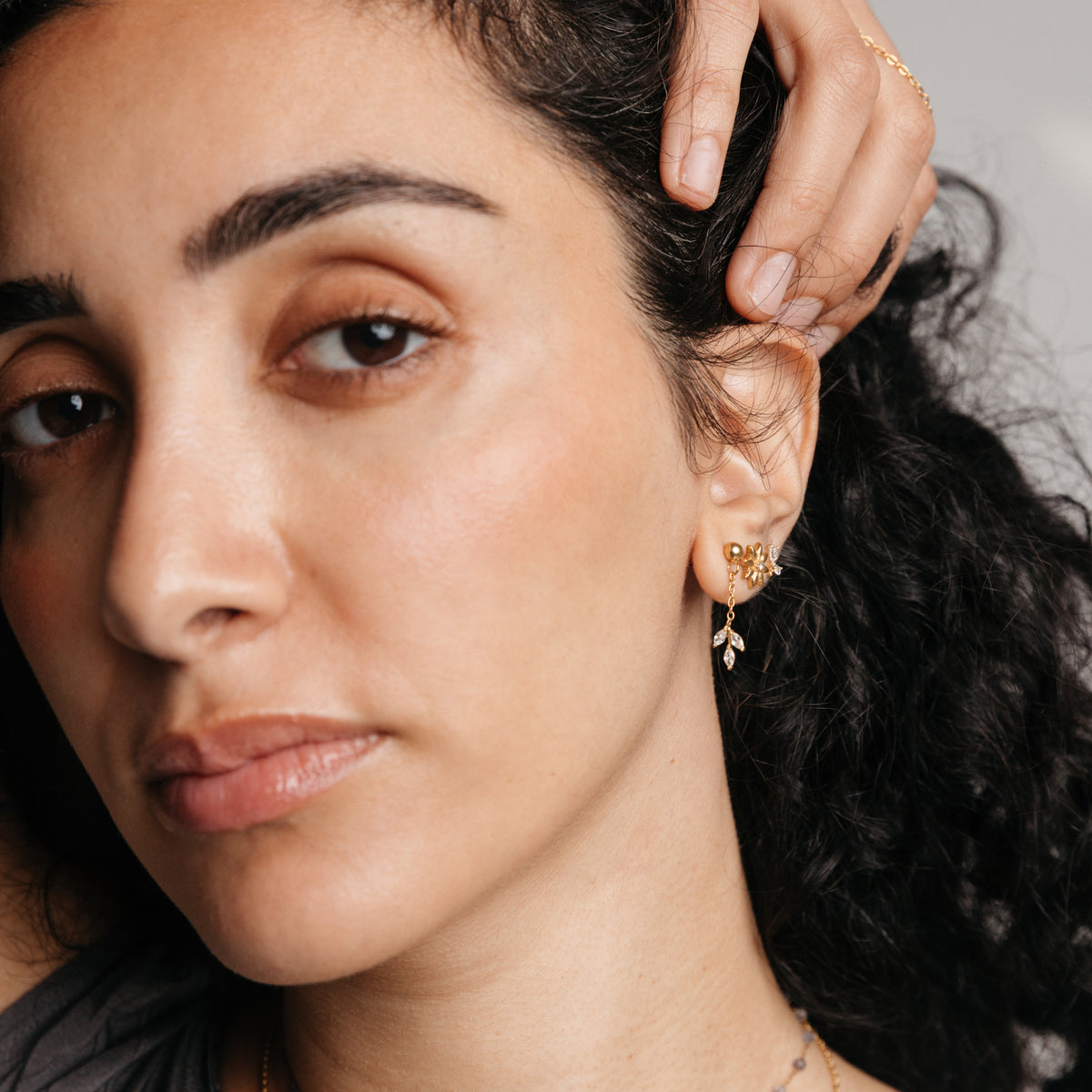 Model styled in 18k gold-plated Nominal jewelry featuring an ear stack with the Pavé Raining Olive Branch Drop Earrings, Bezel Bloom Studs, and Pavé Olive Branch Studs.