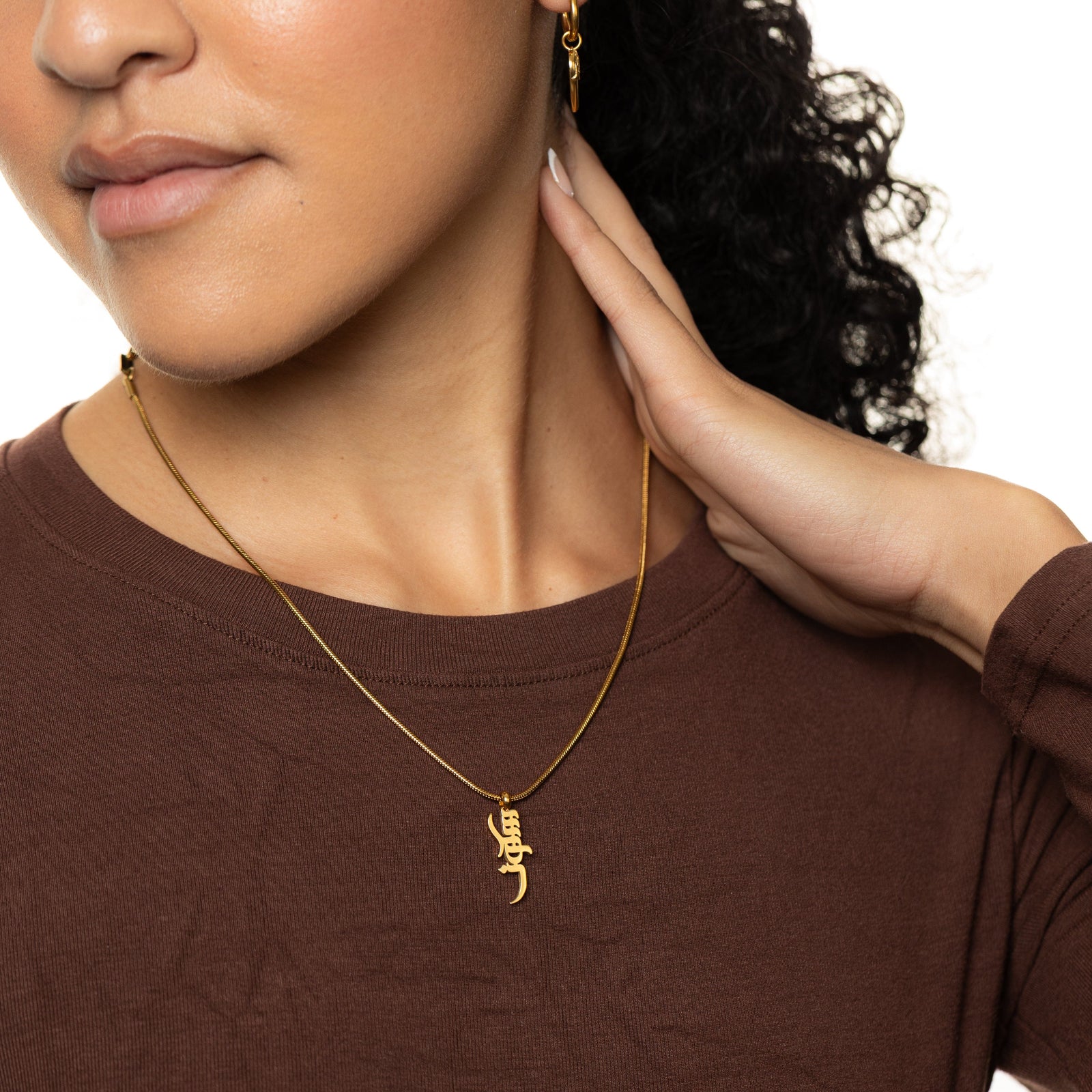Close-up of a person wearing a gold peace of mind necklace with a pendant on a white background