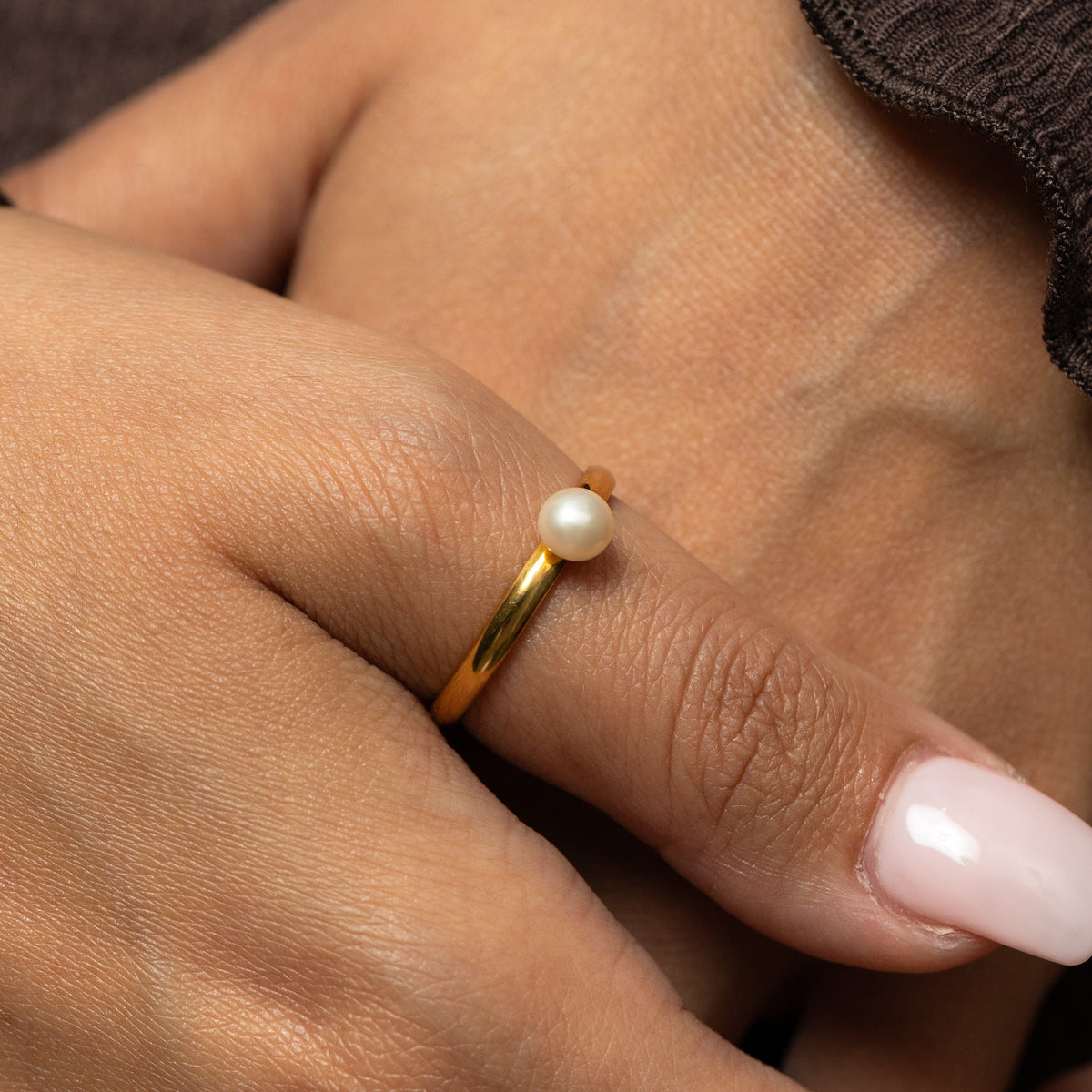 Gold pearl ring worn on a person's thumb.