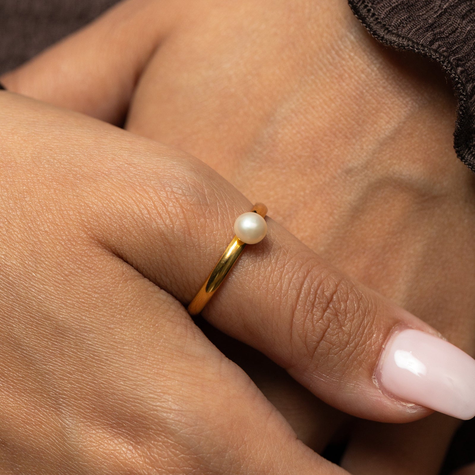 Gold pearl ring worn on a person's thumb.
