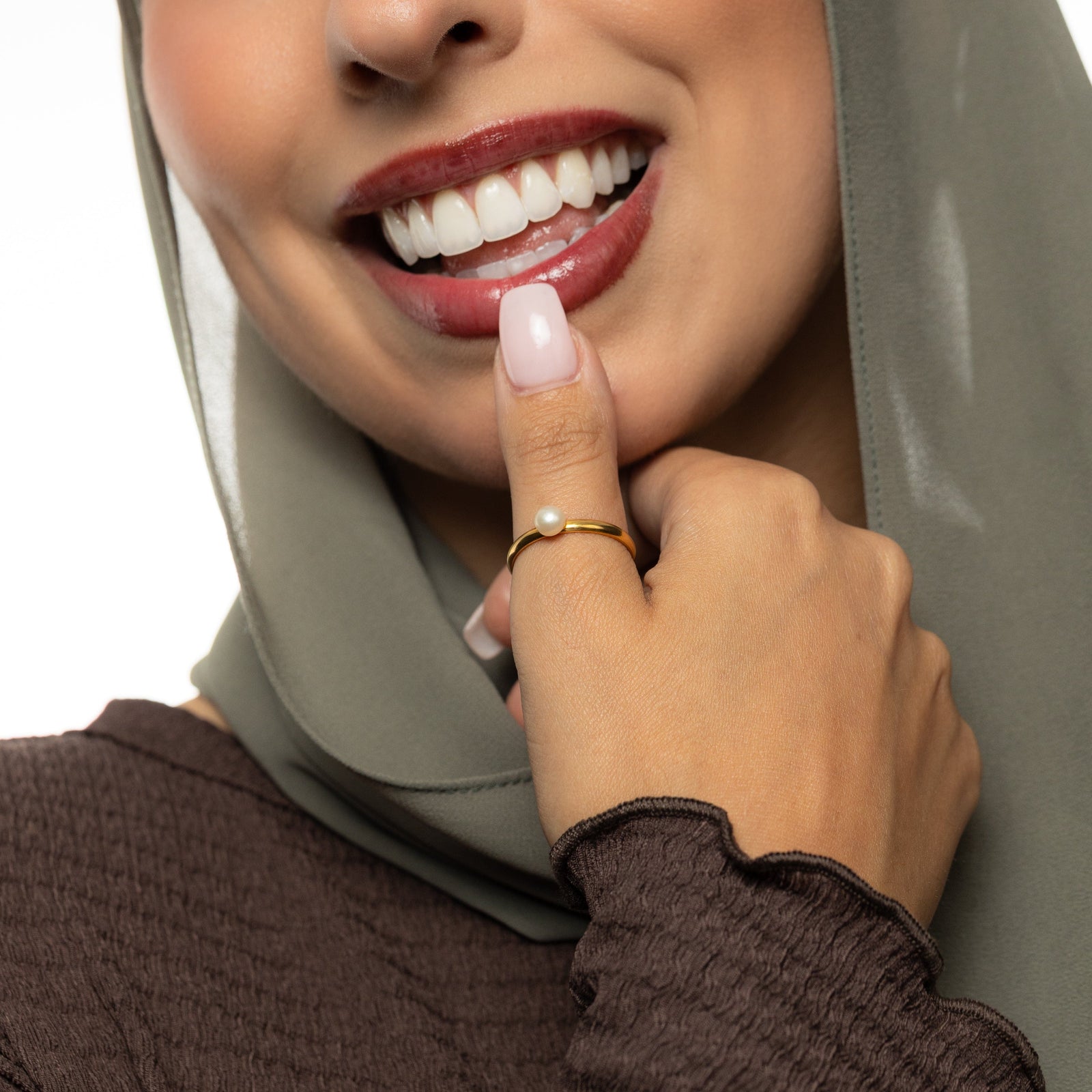 Woman wearing a hijab with a close-up of her hand, Gold pearl ring worn on her thumb.