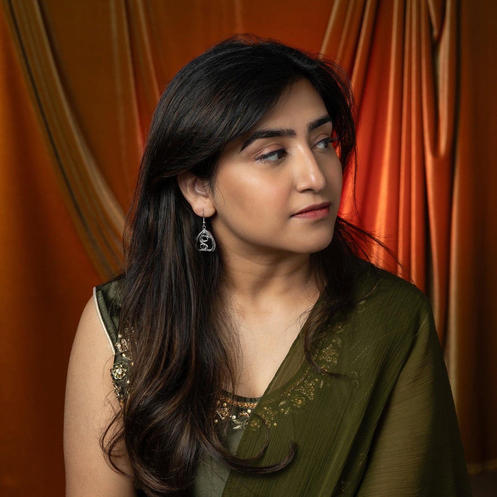 A person is shown in profile, wearing silver "Peepal Earrings" and a silver necklace. Their hand, with henna, is near their face. The background includes a red car interior.