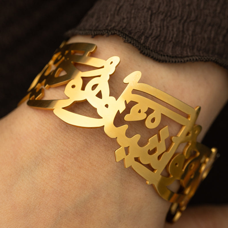 The gold ‘Perhaps you dislike something which is good for you’ Calligraphy Cuff pimage_ showing the open Arabic script design on the wrist.