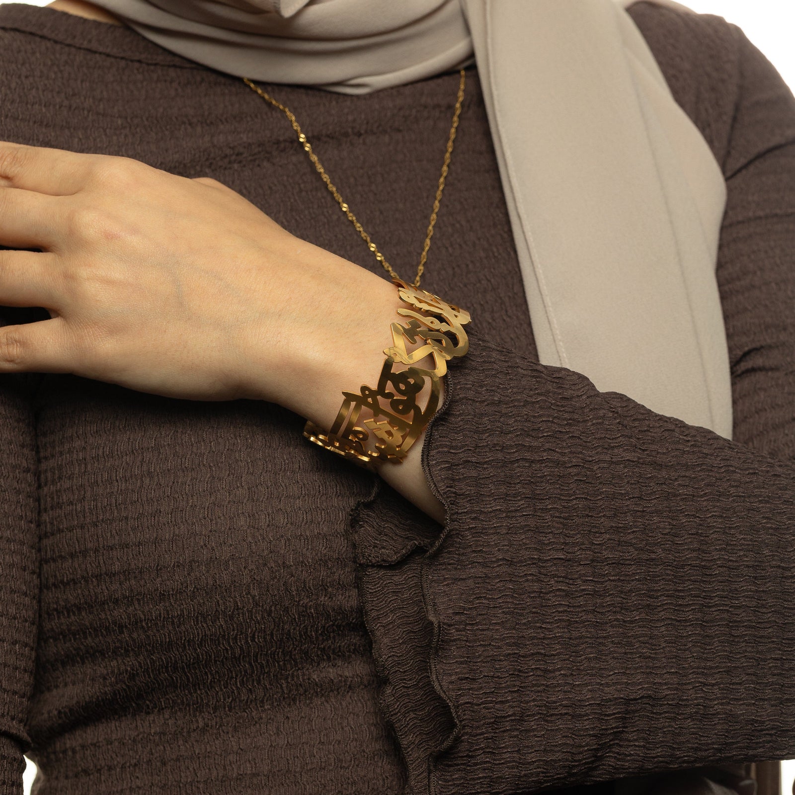 Woman wearing the gold ‘Perhaps you dislike something which is good for you’ Calligraphy Cuff, showing the open Arabic script design on the wrist.