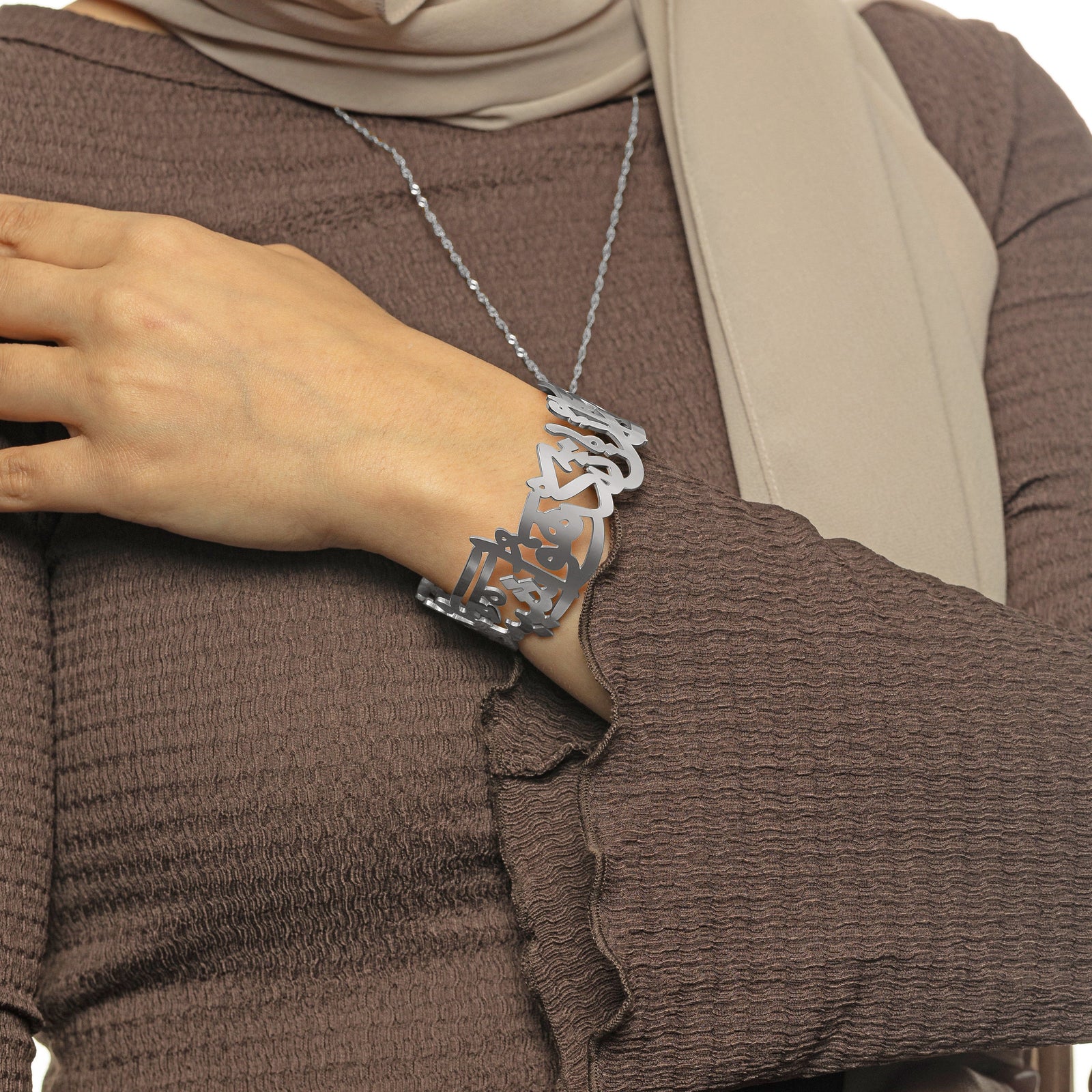 Woman wearing the silver ‘Perhaps you dislike something which is good for you’ Calligraphy Cuff, styled with a brown sleeve.