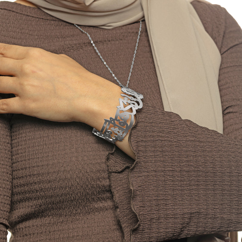 Woman wearing the silver ‘Perhaps you dislike something which is good for you’ Calligraphy Cuff pimage_ styled with a brown sleeve.