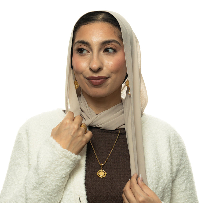 Model wearing the gold “Perhaps you dislike what's good for you” Coin Necklace pimage_ styled with a beige hijab and white jacket.