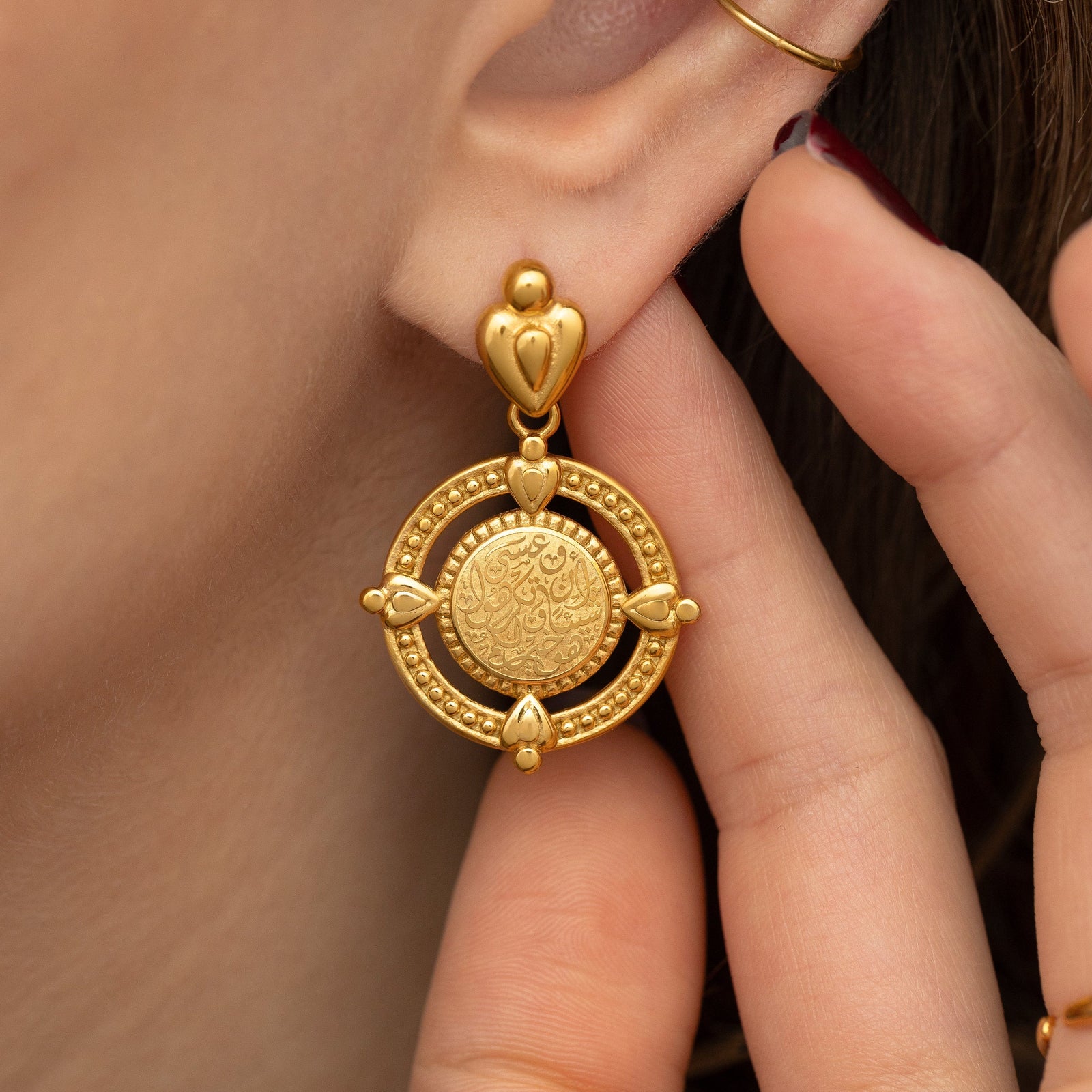 Close up photo of the model touching their left ear wearing the gold "Perhaps you dislike what's good for you" Coin Earrings.