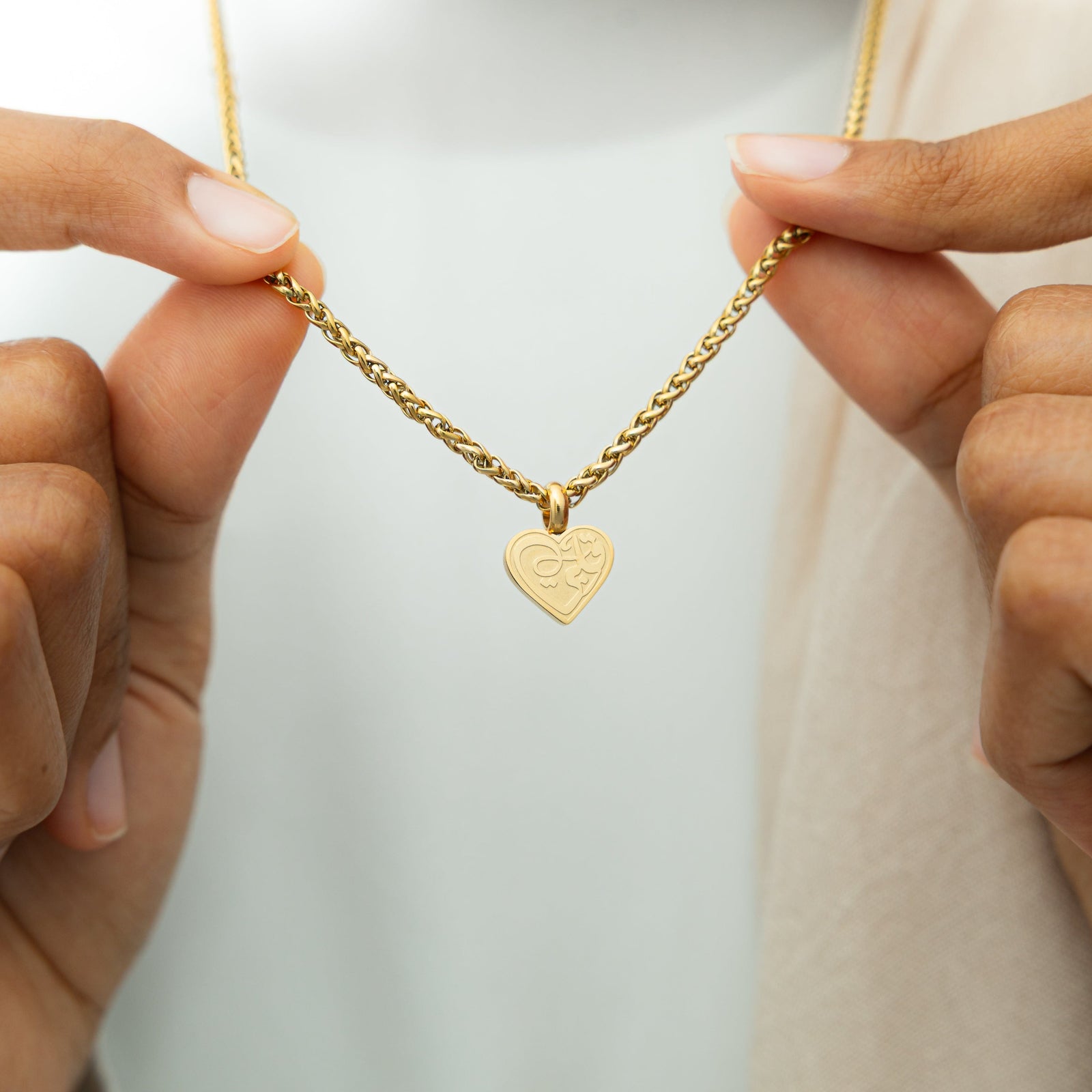 Close up of the gold "Piece of Me" Daughter Necklace as the model holds the chain to show the pendant.