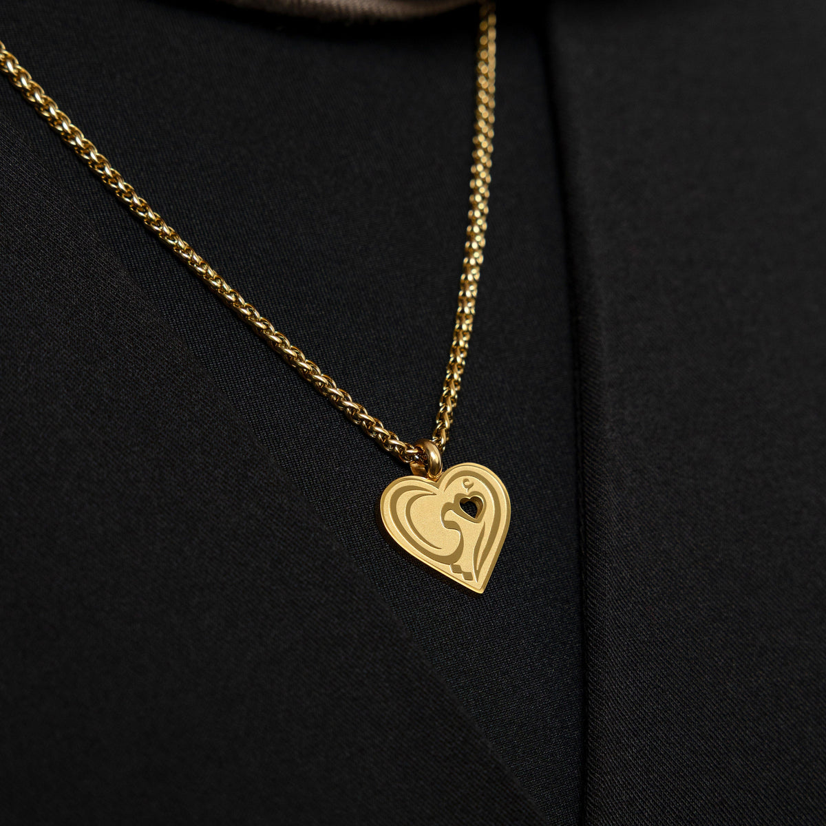 Close up of the gold "Piece of Me" Mama Necklace against the black fabric of the model's shirt.