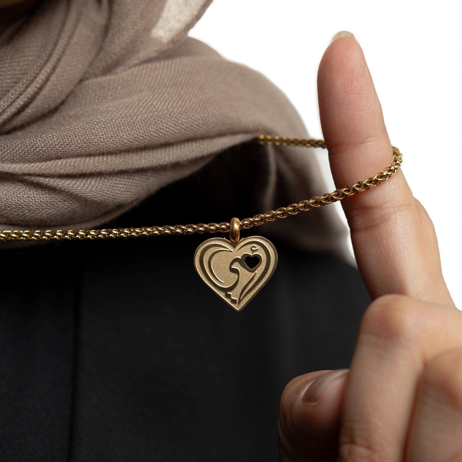 Close up of the gold "Piece of Me" Mama Necklace as the model lifts the gold chain to show its pendant.