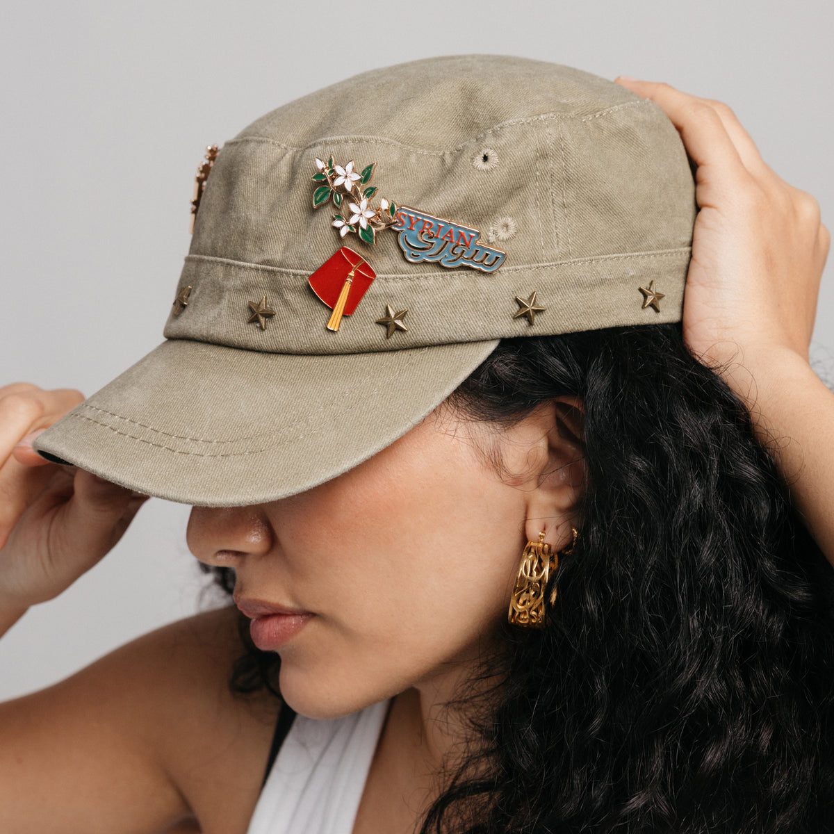 18k gold-plated cultural enamel pins and gold hoop earrings styled on a model's hat.