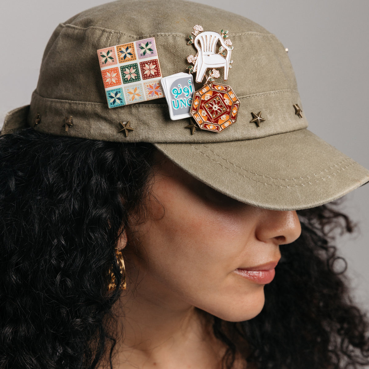 18k gold-plated cultural enamel pins and gold hoop earrings styled on a model's hat.