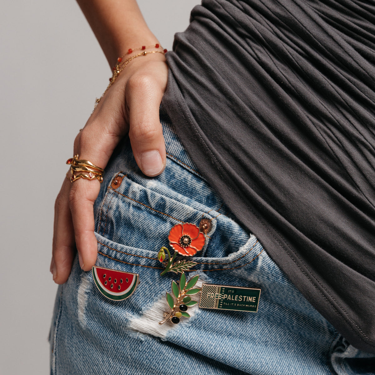 18k gold-plated Palestinian enamel pins and gold jewelry styled on denim jeans.