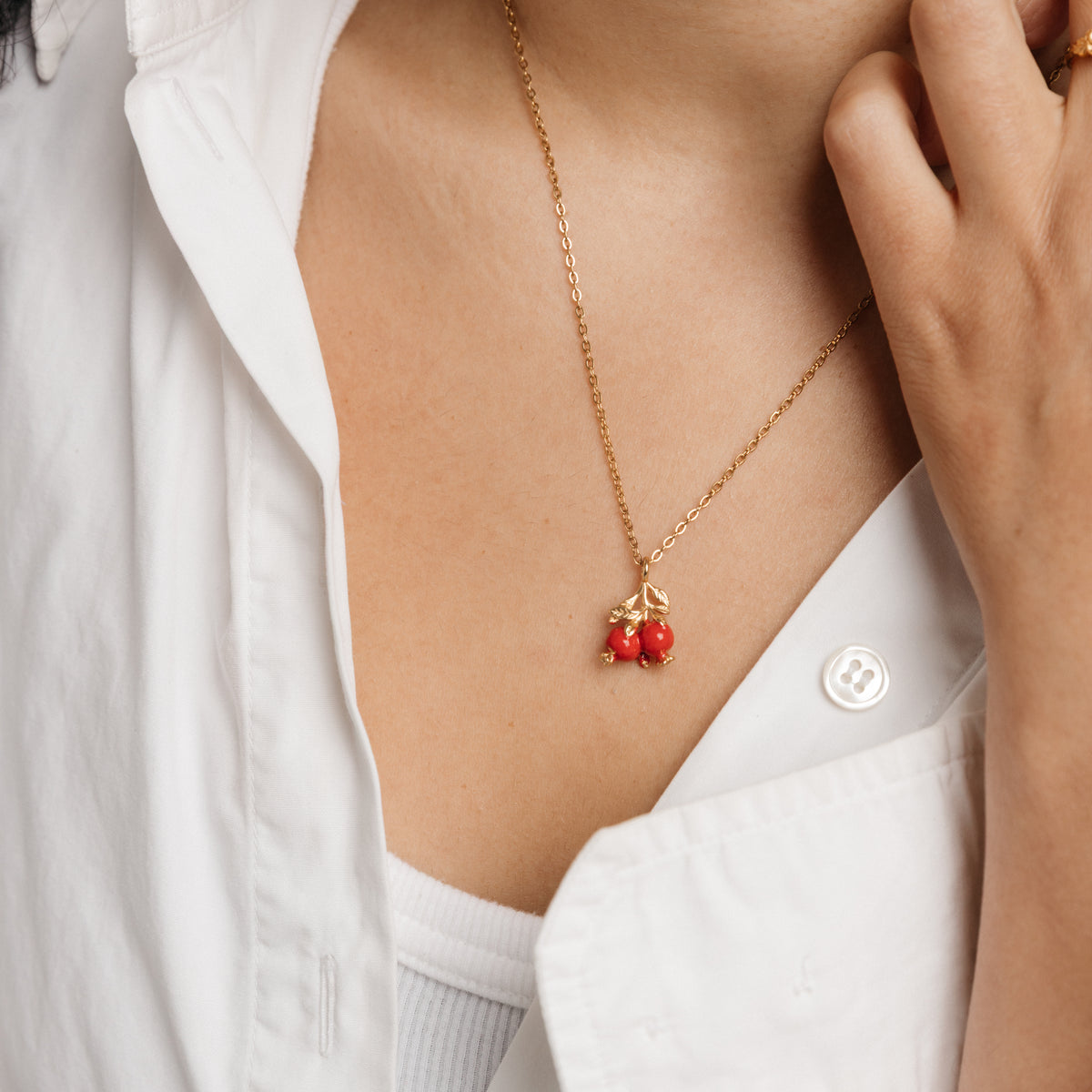 On-model view of the Pomegranate Necklace by Nominal, featuring an 18k gold-plated chain and vibrant red pomegranate pendant styled with an open white collared shirt.