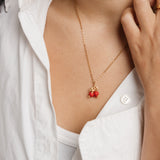 On-model view of the Pomegranate Necklace by Nominal, featuring an 18k gold-plated chain and vibrant red pomegranate pendant styled with an open white collared shirt.