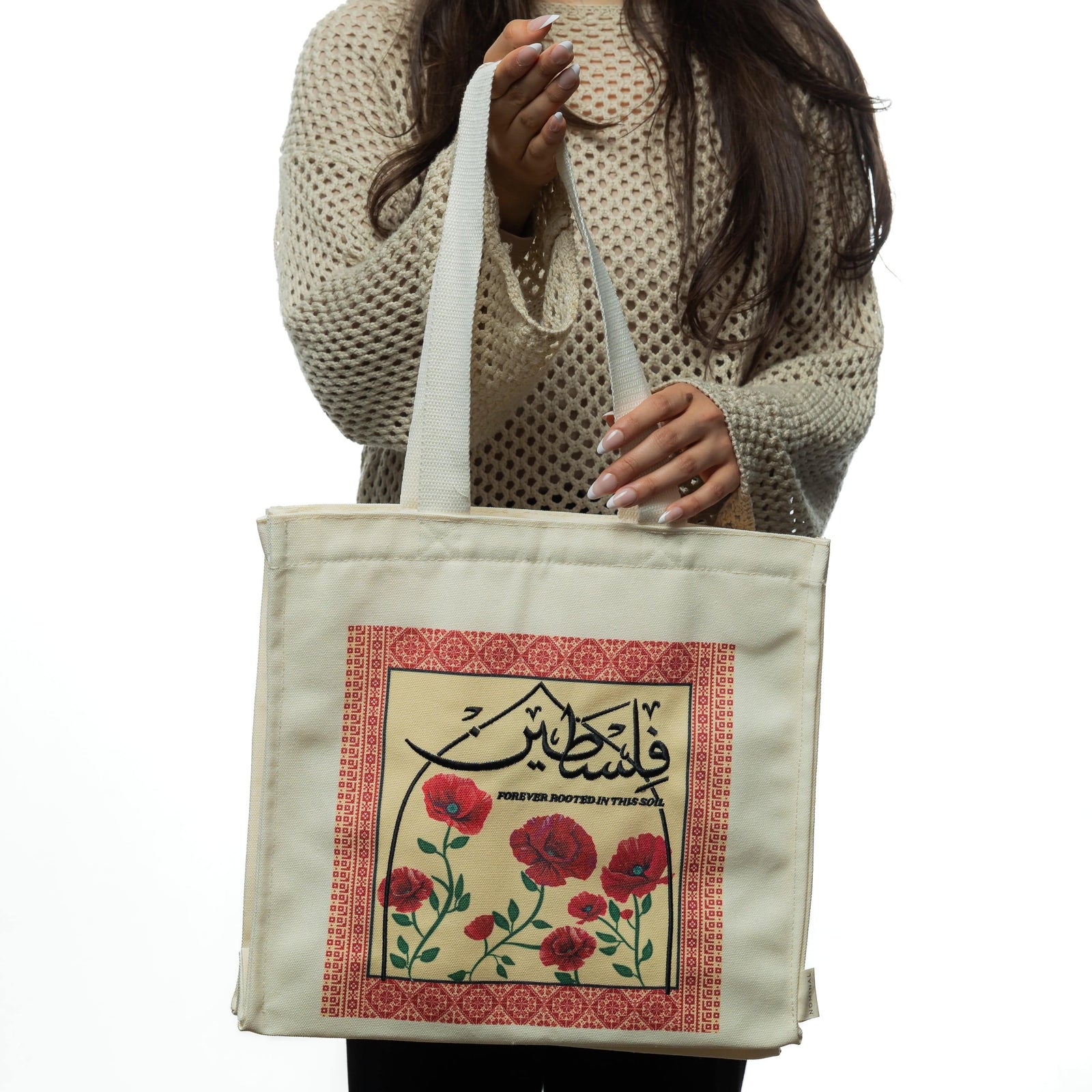 Woman in a beige textured sweater holding the Poppy Tatreez Palestine tote by the handles.