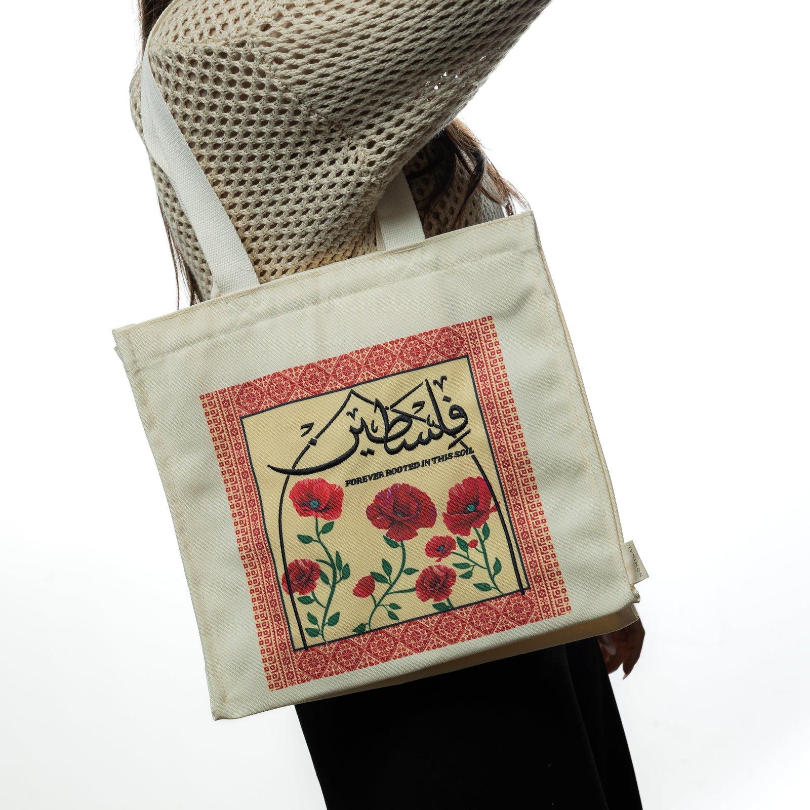 Woman wearing the Poppy Tatreez Palestine tote bag over her shoulder. The side view highlights the tote’s boxy structure and artistic front panel.