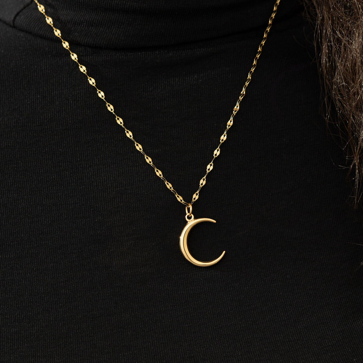 The gold Premium Crescent Necklace resting against the black fabric of the model's shirt.