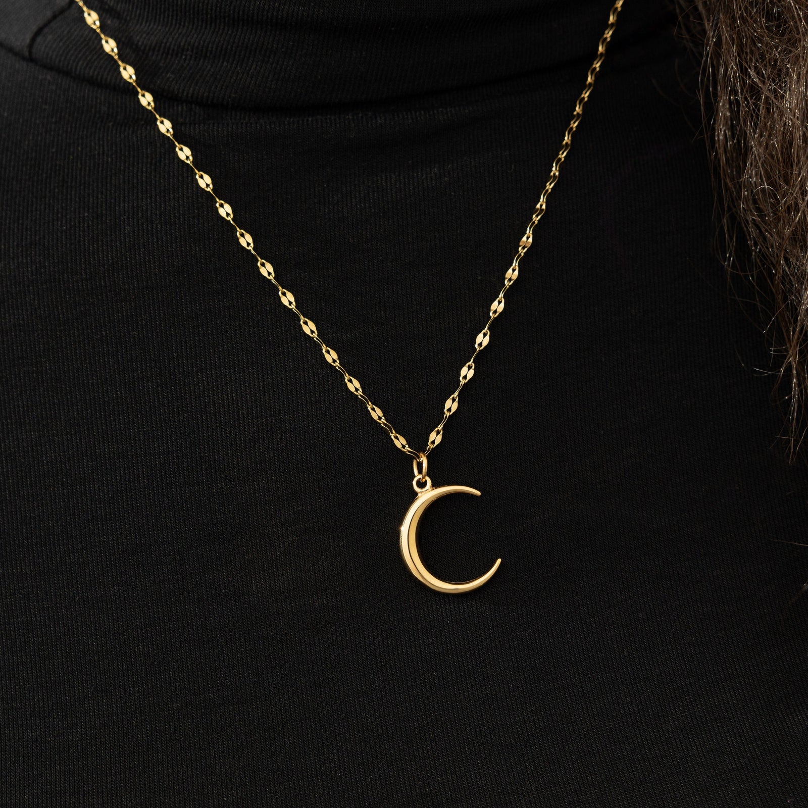 The gold Premium Crescent Necklace resting against the black fabric of the model's shirt.