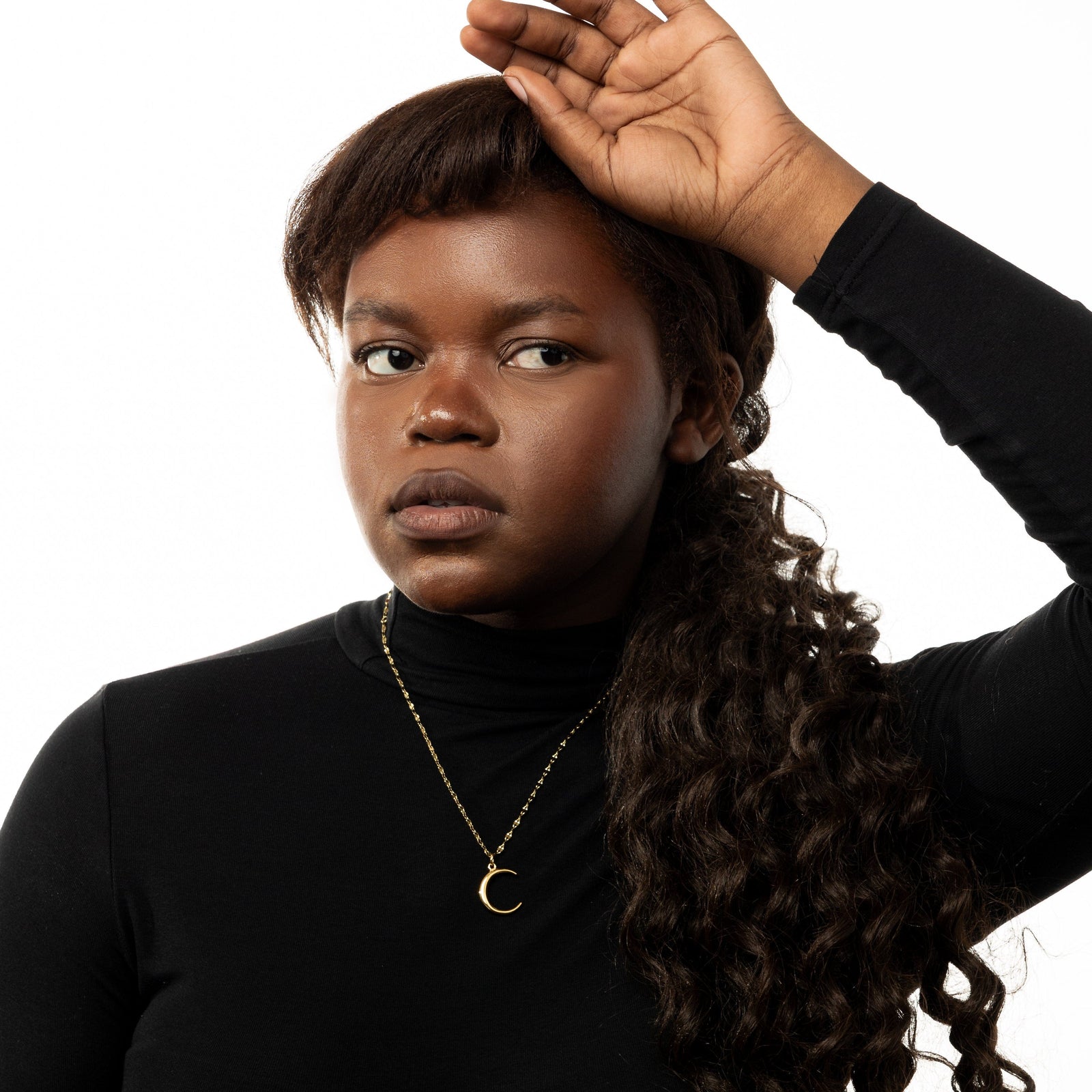 Photo of the model resting their left hand on their head. The model is wearing the gold Premium Crescent Necklace.